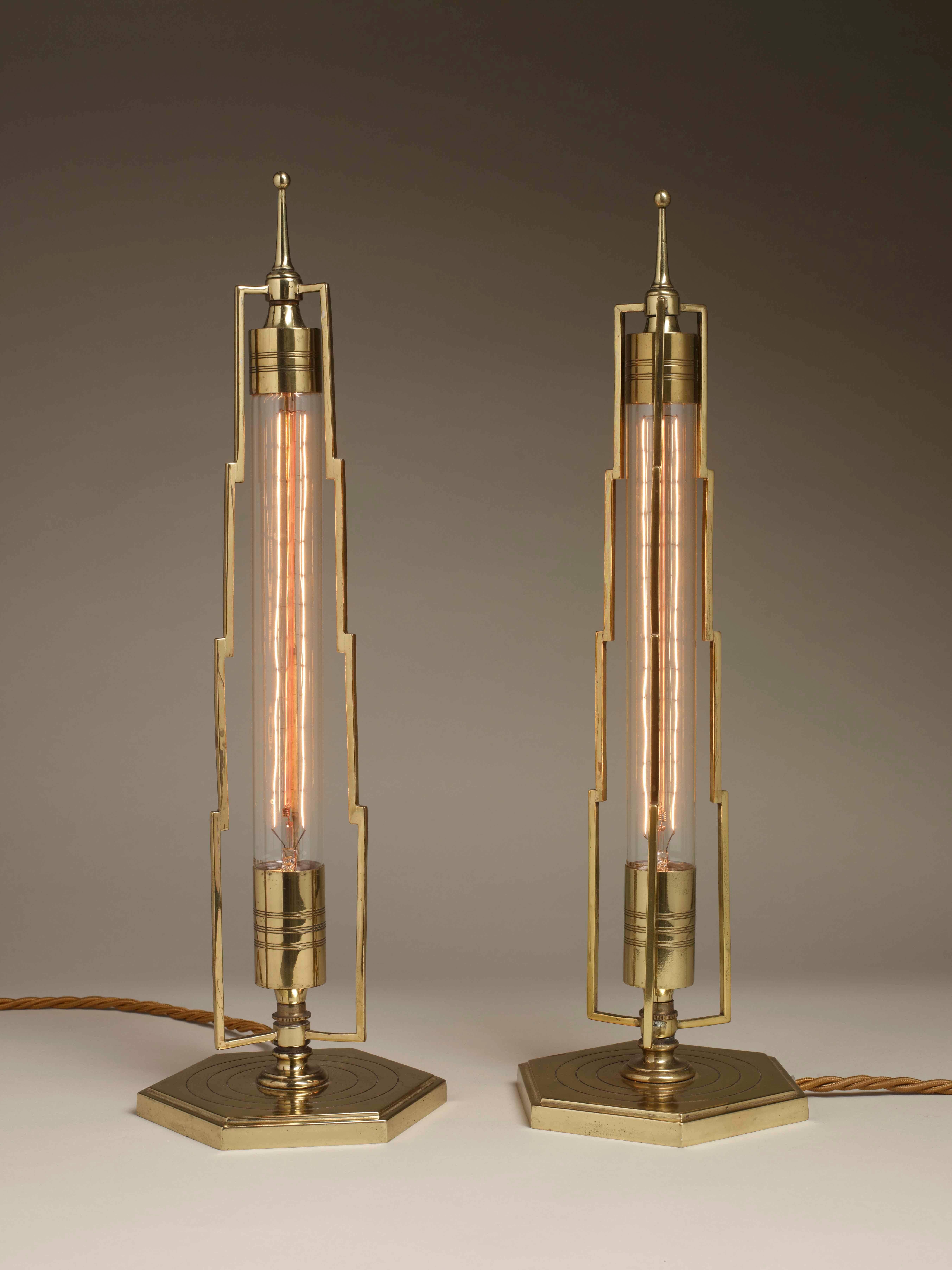 An unusual pair of Art Deco futuristic tube table lamps.

With opaline glass with collars of engraved polished brass, inside a framework of stepped brass tapering to a pointed finial spire. Standing on a hexagonal base with further engraved