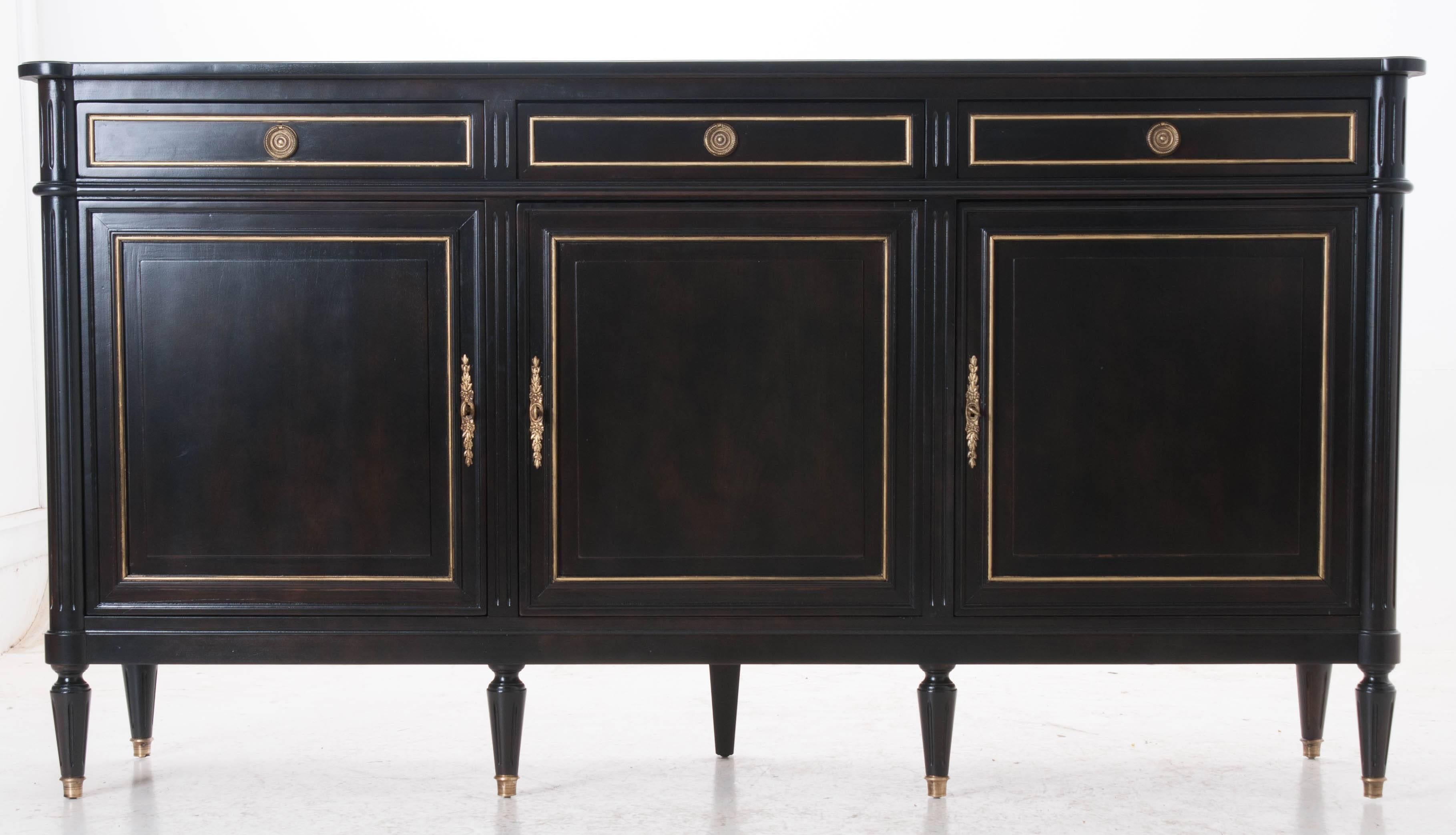 This absolutely stunning Louis XVI style enfilade has been expertly refinished in a matte black ebony with gold trimmed panels on front doors, drawers and side panels. Gilt brass hardware and gilt brass capped feet continue the gilt with ebony