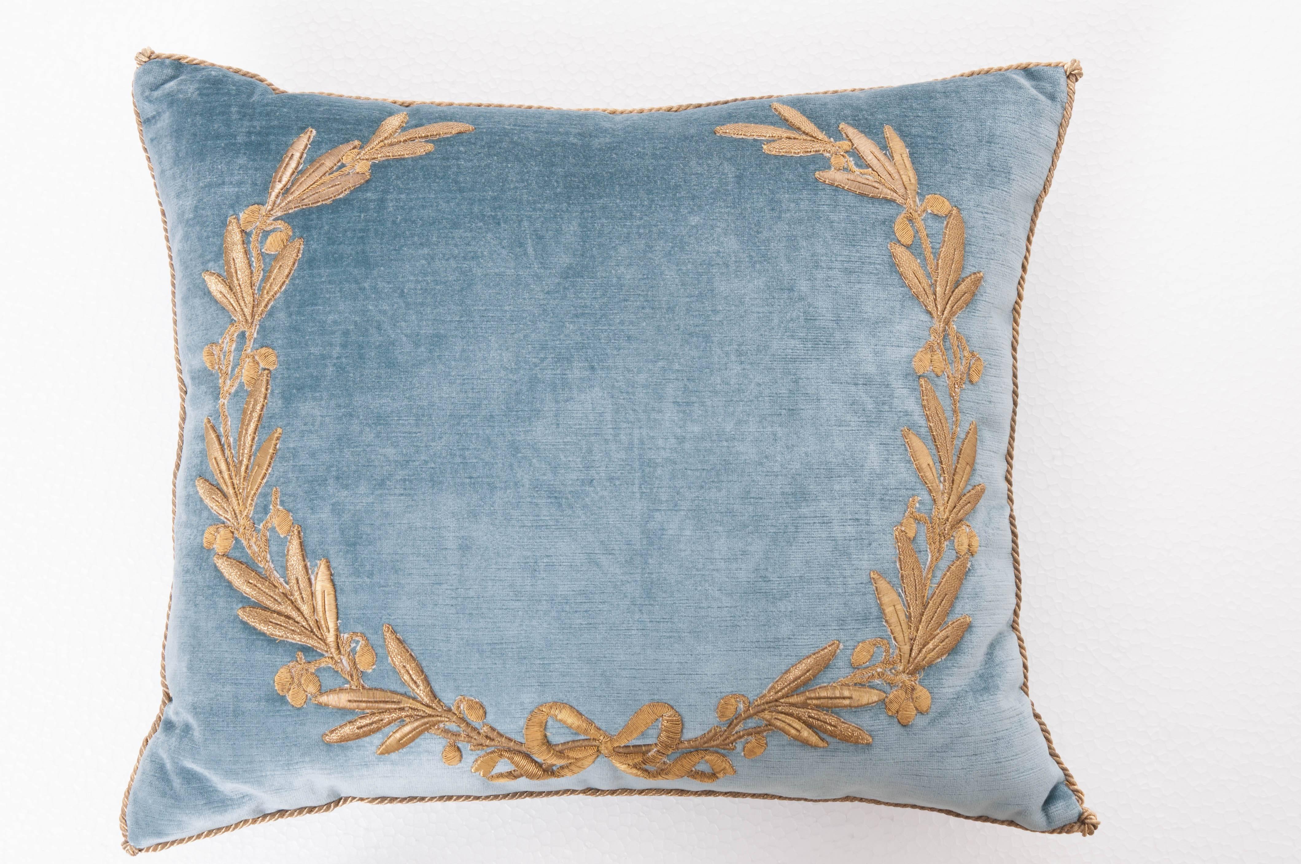 Antique European raised gold metallic embroidery of a neoclassical wreath with a bow on Wedgewood blue velvet. Hand trimmed with vintage gold cording knotted in the corners. Down filled.