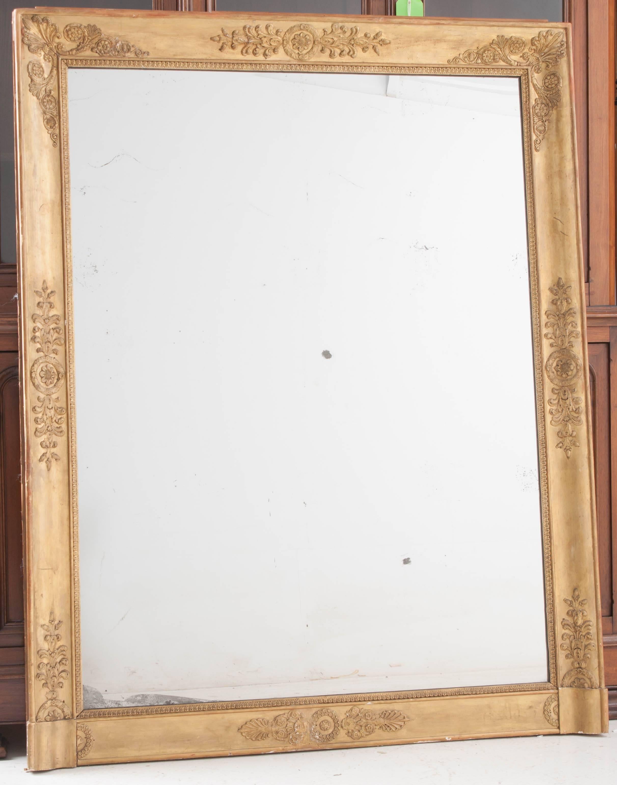 This 19th century Empire period mirror boasts exquisite gold gilt and neoclassical carvings that surround its original glass. The original mercury glass has magnificent foxing and sparkles. A warm patina envelops the entire mirror, adding to its