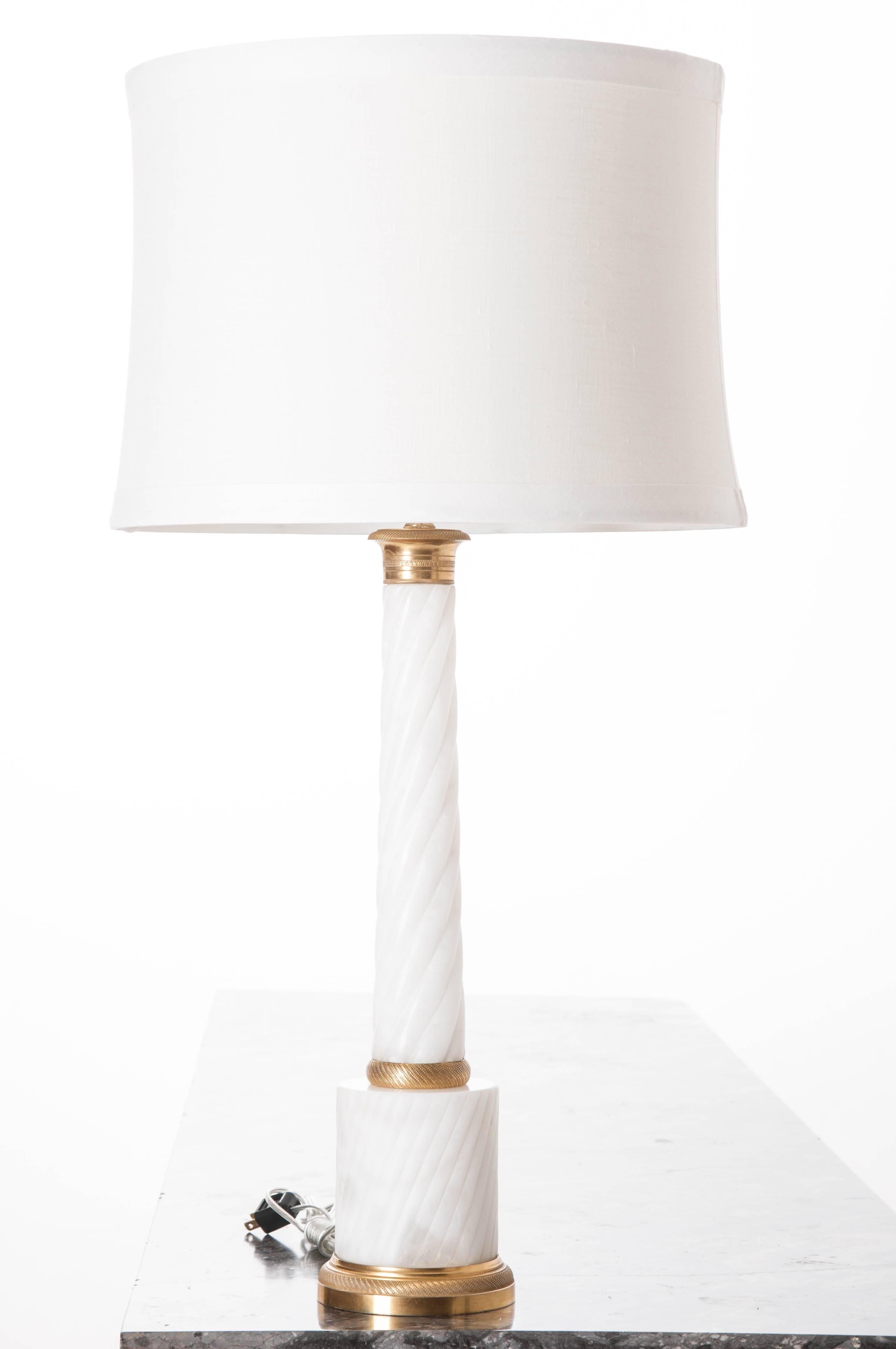 This exceptional lamp is made from a carved, twisted, white marble column of the Empire style. The column is capped with a brass capital and sits on a larger, white marble cylinder. The whole rests on a brass base. Custom ivory linen shade.