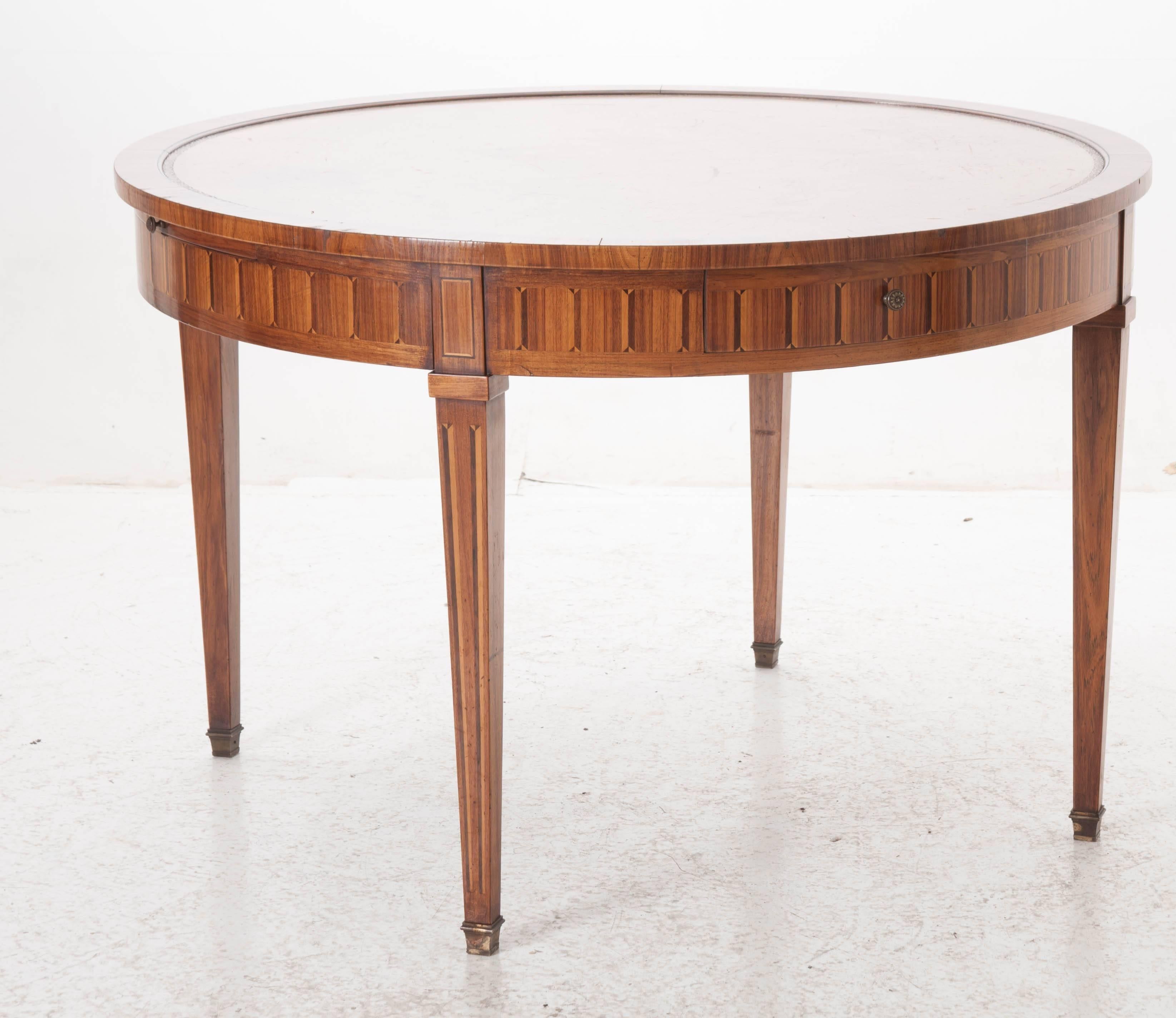 An outstanding round Directoire table from 19th century, France. This leather top table exhibits supremely executed rose and satinwood inlay found in its apron as well as its tapered legs. The apron also houses two drawers and two leather top slides