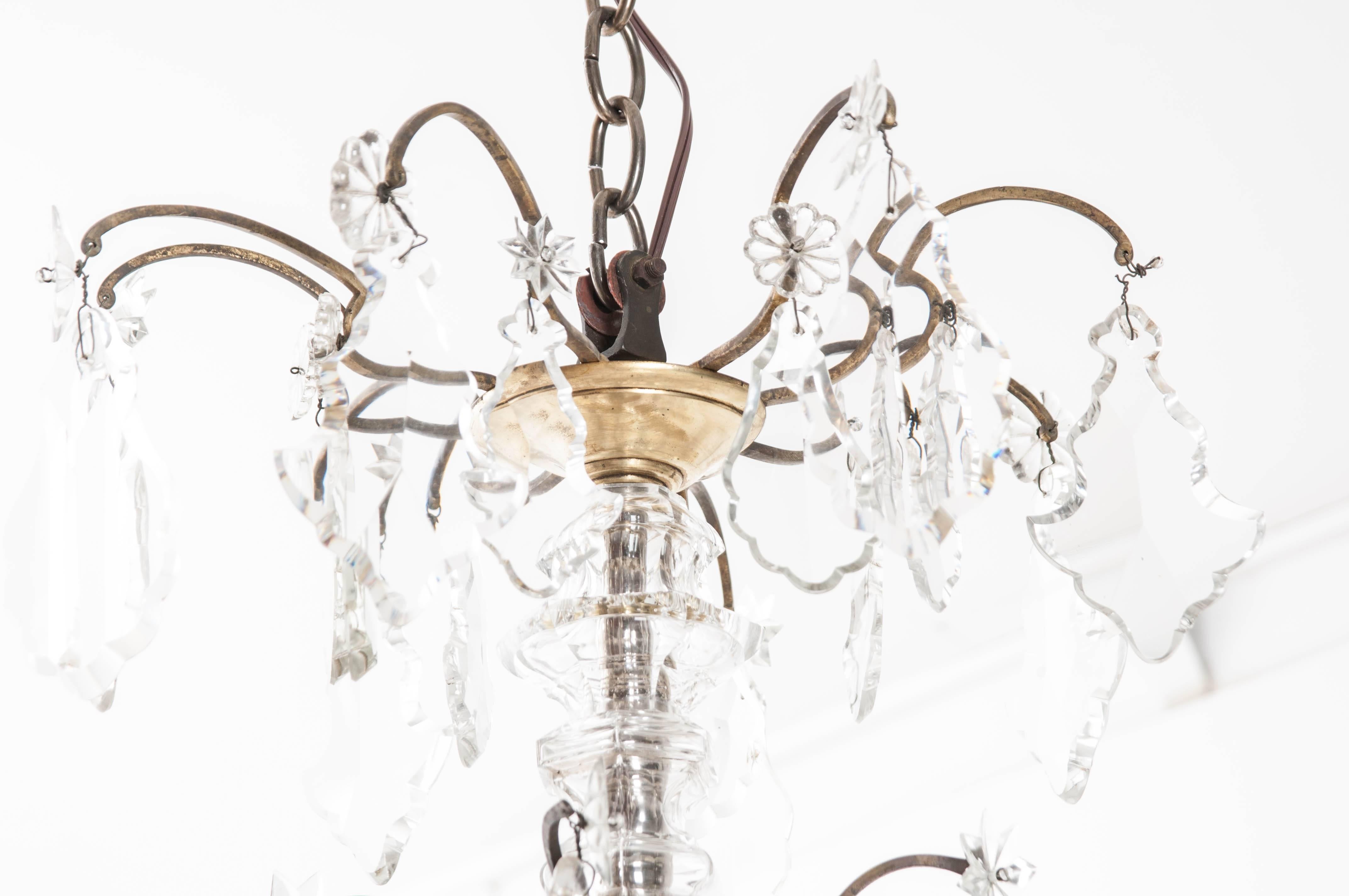 This exquisite French chandelier has 12 lights and is thoroughly adorned with beautiful drop pendant crystals. These are surmounted by crystal stars and rosettes intended to conceal the attachment point between crystal and metal frame. The birdcage