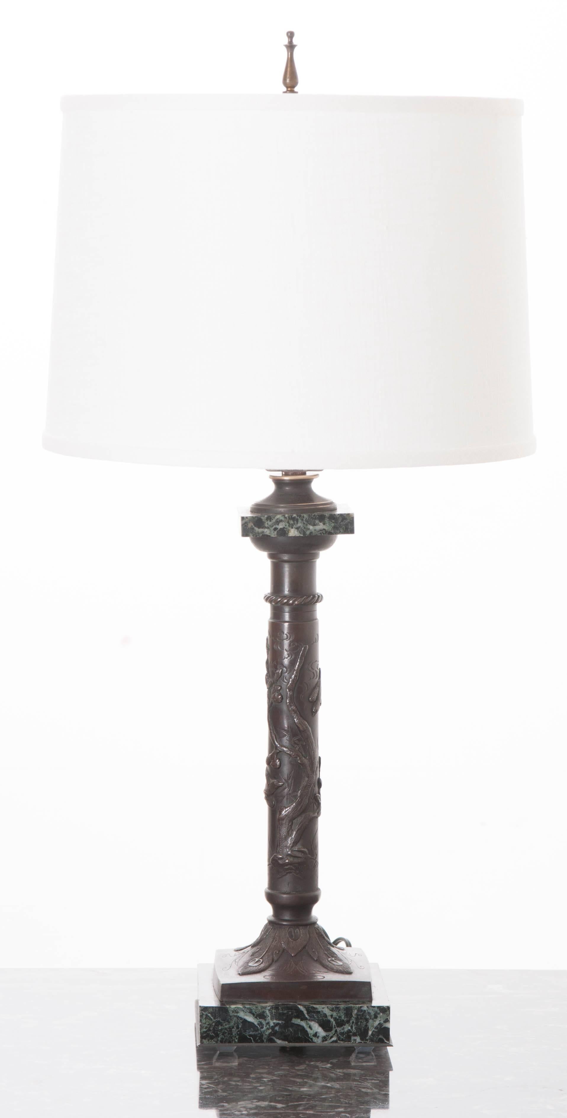 This small, decorative table lamp has been fashioned using an ornate bronze column that rests on a square marble base. The column's shaft features a gnarly tree with sparrows circling in pursuit of its precious fruit. The column's base is decorated