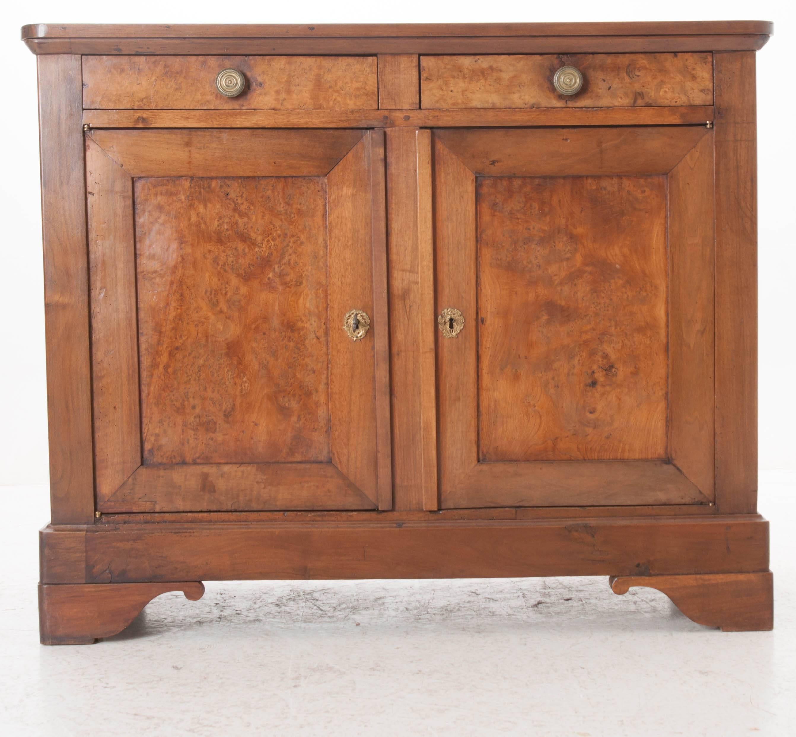 A stunning pair of walnut Louis Philippe buffets from 19th century France. Crafted from solid walnut, each buffet is outfitted with two drawers set above two doors that feature handsome solid burl walnut facades. The drawers have round, decorative