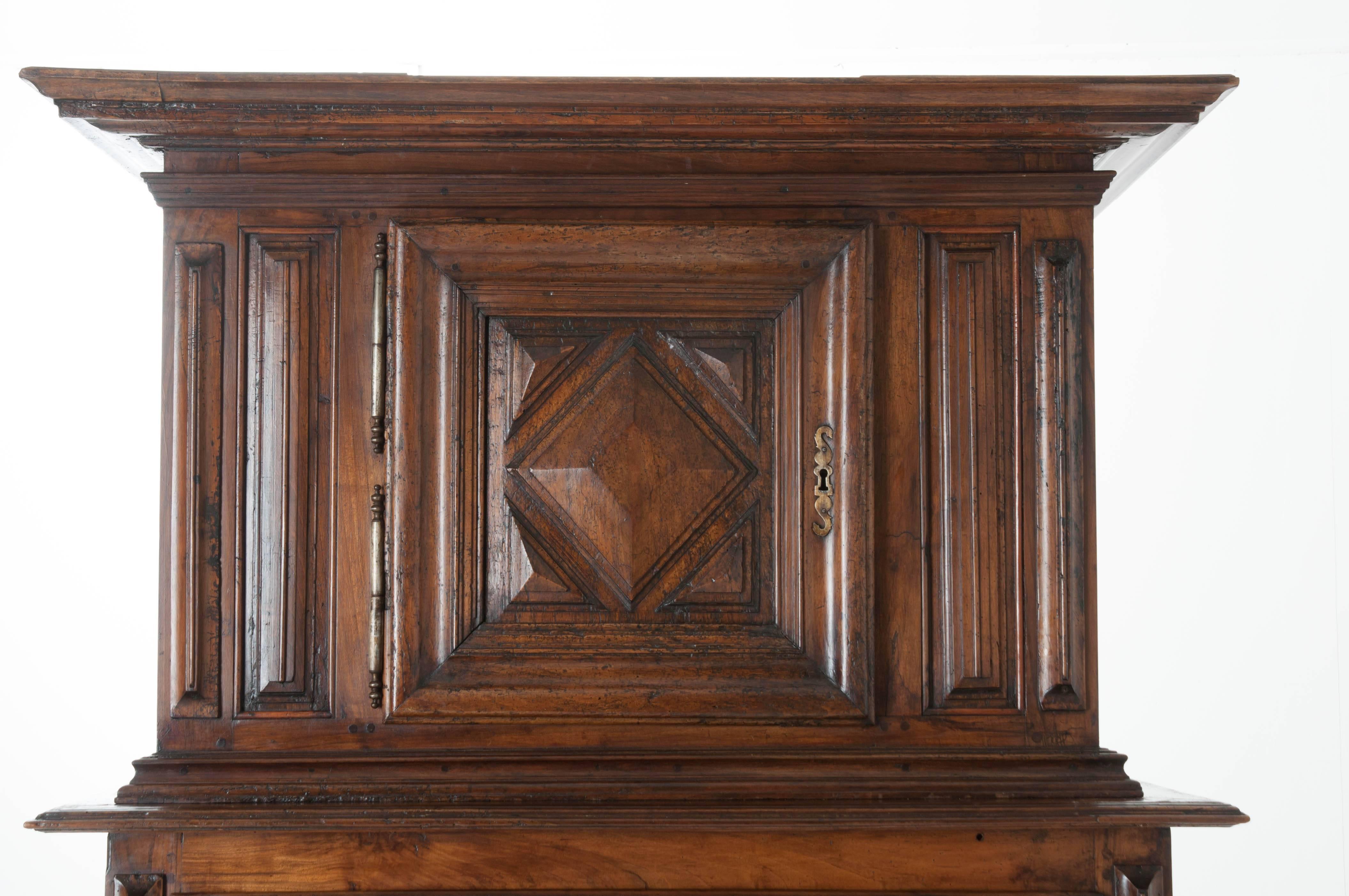 A nearly 400 year old walnut buffet a deux corps from 17th century, France. This Louis XIII period piece features two heavy, lockable doors with geometric carvings in deep relief. These doors are hung on barrel hinges and are separated by a lockable