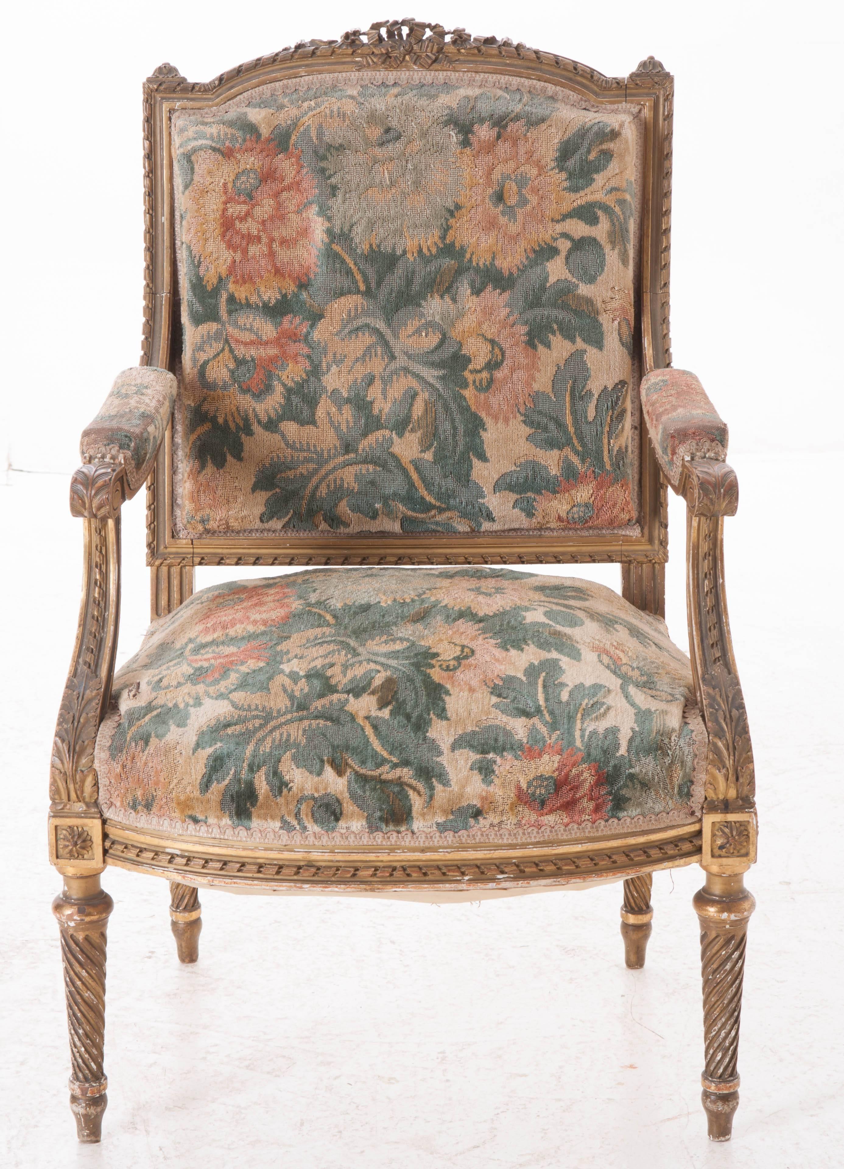 A gorgeous French gold gilt fauteuil that still has its original tapestry upholstery. This Louis XVI style chair features extensive intricate carvings. Its shaped top rail is crowned with a superbly carved bow which rests atop the twisted ribbon