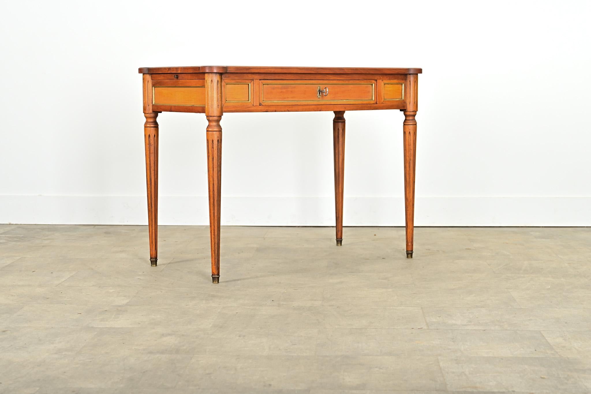 A petite, leather-topped mahogany writing desk dating to the 19th century in the Louis XVI style, with hidden extensions on each side to add occasional surface area. Framed by turreted corners, the leather surfaces of the top are a neutral,