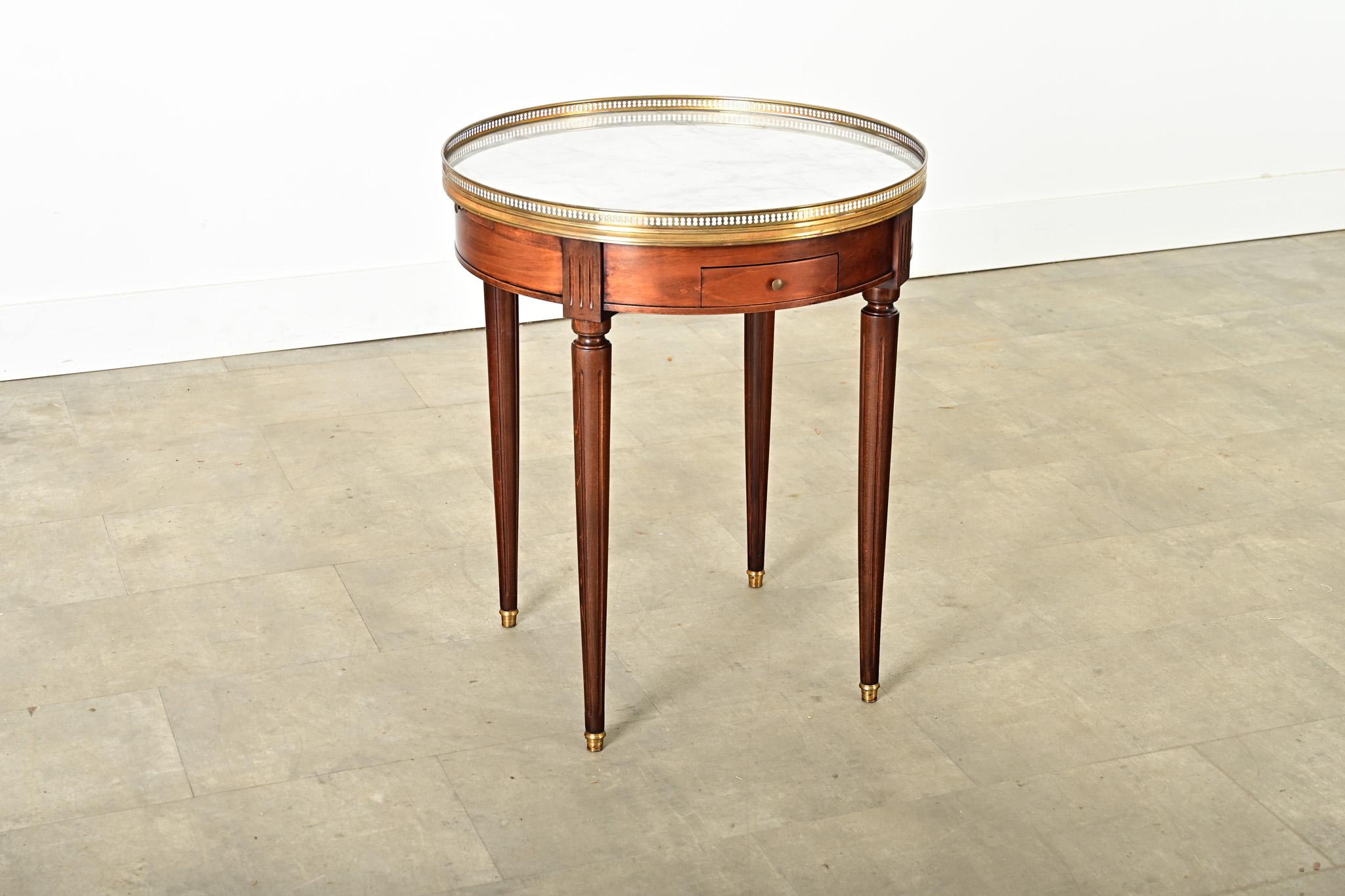 A French Louis XVI style mahogany side table from the 19th century with a white marble top surrounded by a pierced brass gallery and elevated by fluted legs. This timeless table design is a classic example of form & function, made for the popular