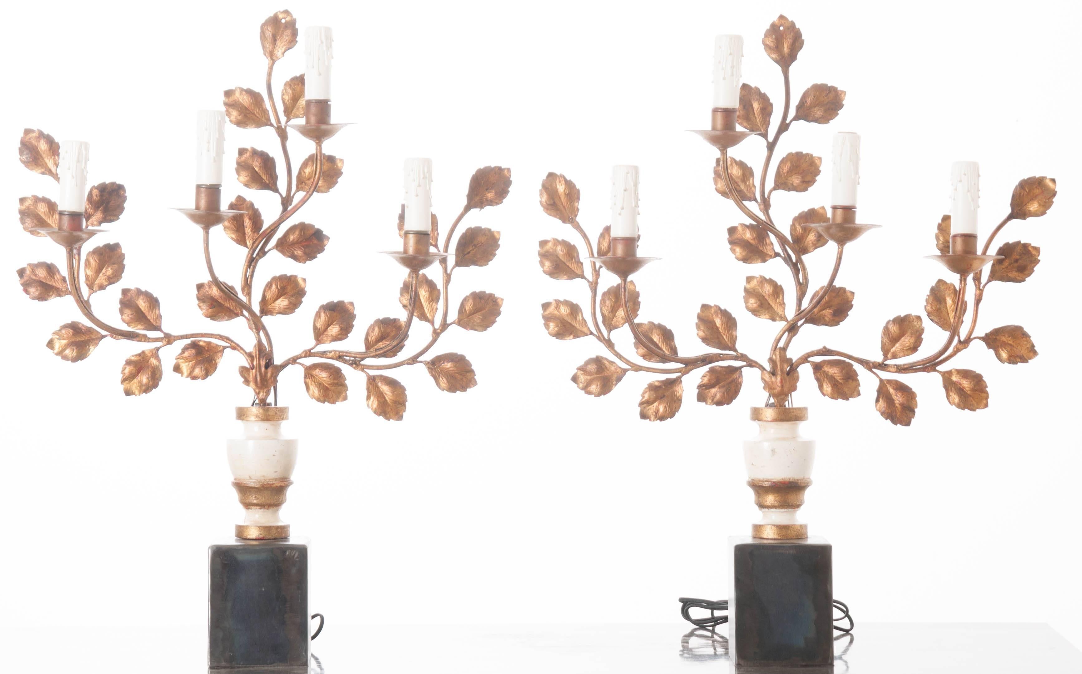 An extraordinary pair of 19th century four-light sconces that have been newly repurposed to function as lamps. Custom metal bases were fabricated to provide a surface to which the antique sconces could be mounted. These exquisite lamps are formed