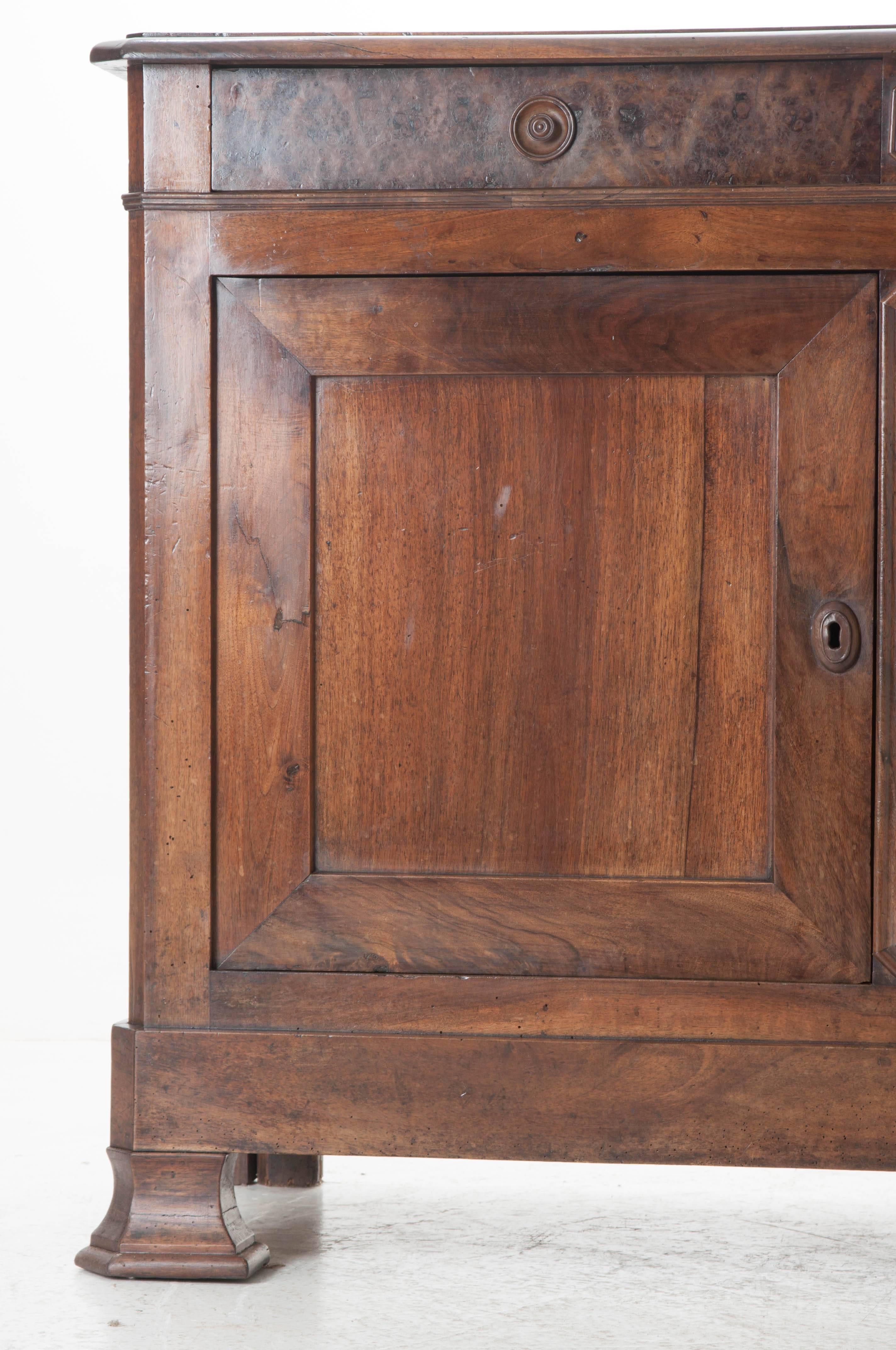 A large 19th century Louis Philippe style walnut buffet with marvelous burl found between the doors as well as on the drawer fronts. Recessed, turned wood knobs grace the two drawers that are set above the two lockable doors. These doors are hung on