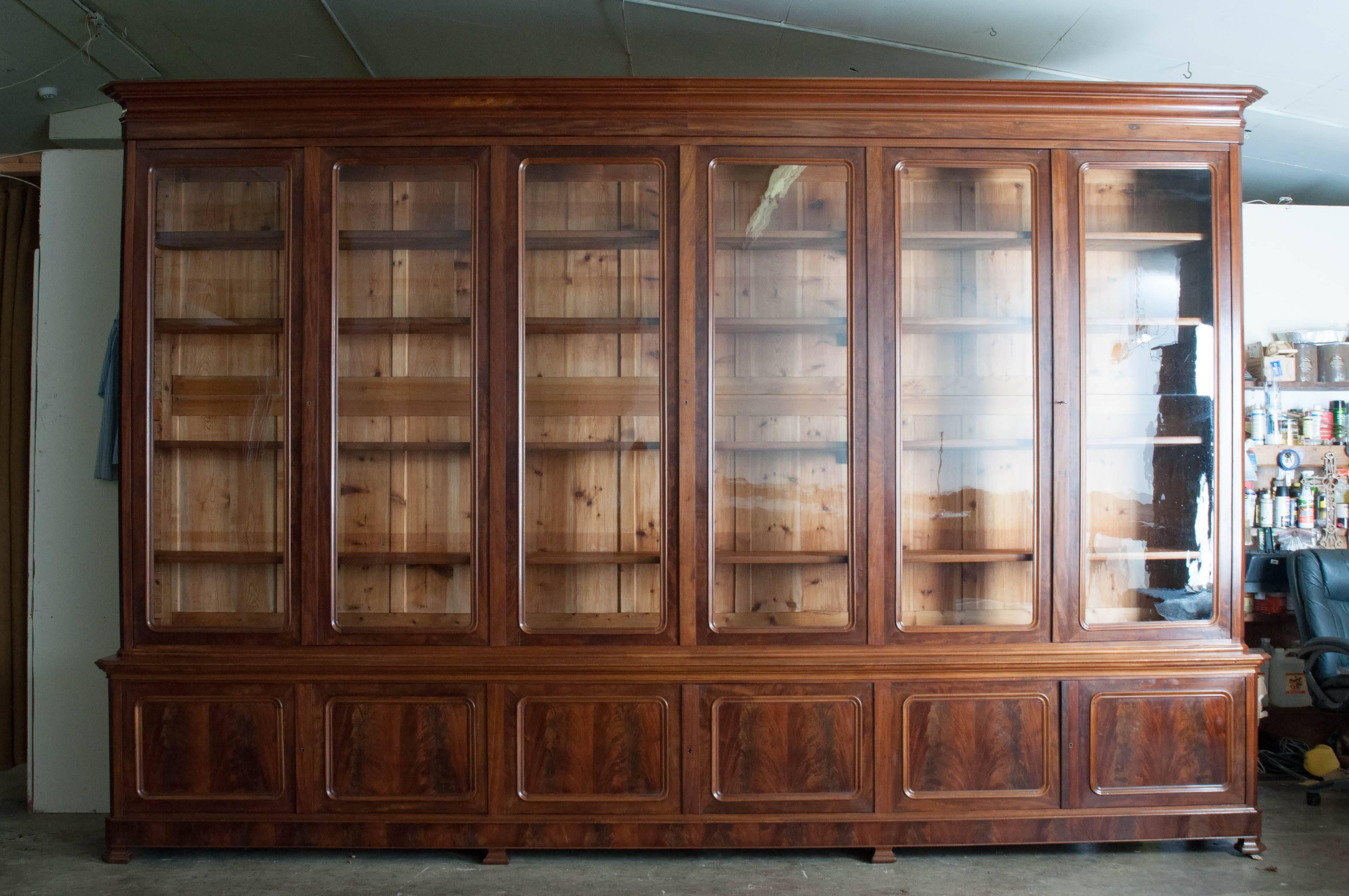 An outstanding large-scale grand bibliotheque in excellent condition. The bookcase stands over 9 feet tall and is over 14 feet long. The top and base do come apart, however, the base and crown remain one long, solid piece. Beautifully figured