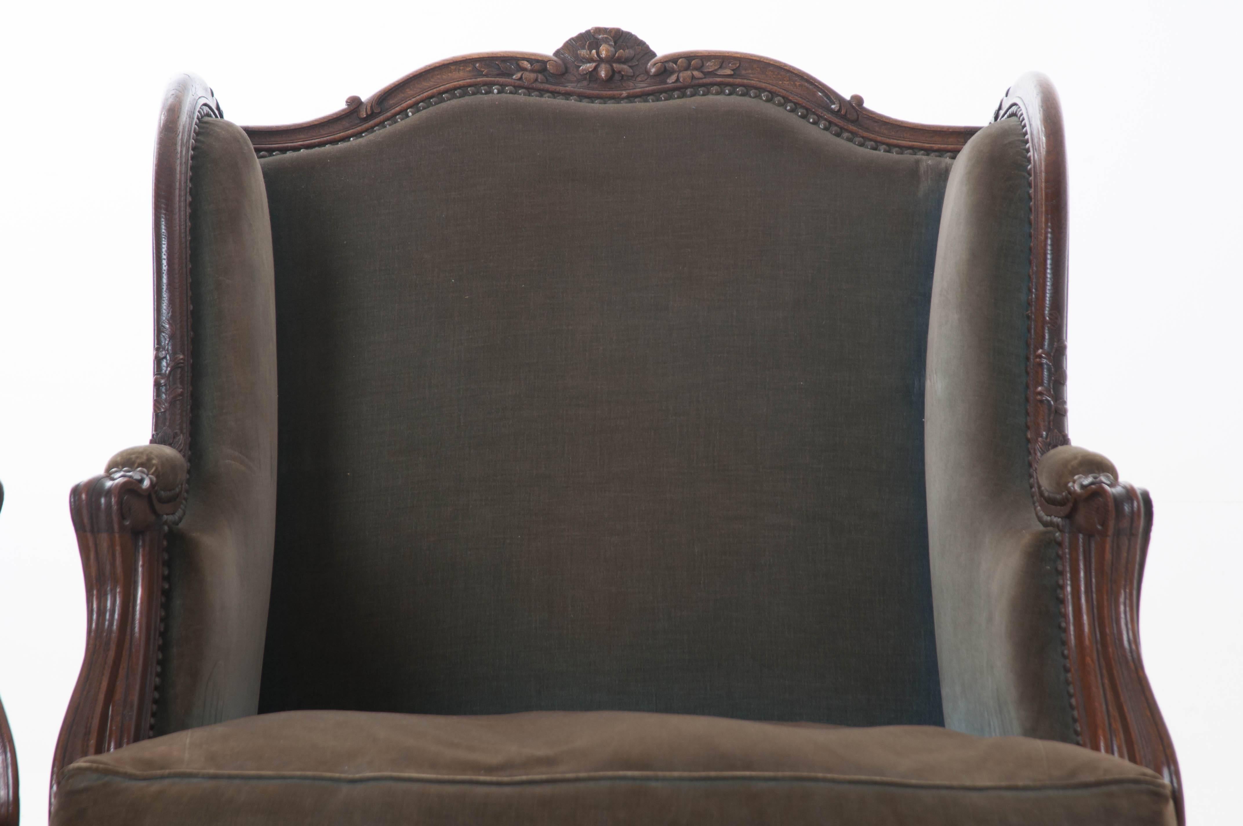A massive pair of extraordinarily handsome carved French oak Louis XV style upholstered bergeres from the 19th century. In need of reupholstering, these large chairs are adorned with truly remarkable carvings that can be found on nearly every inch