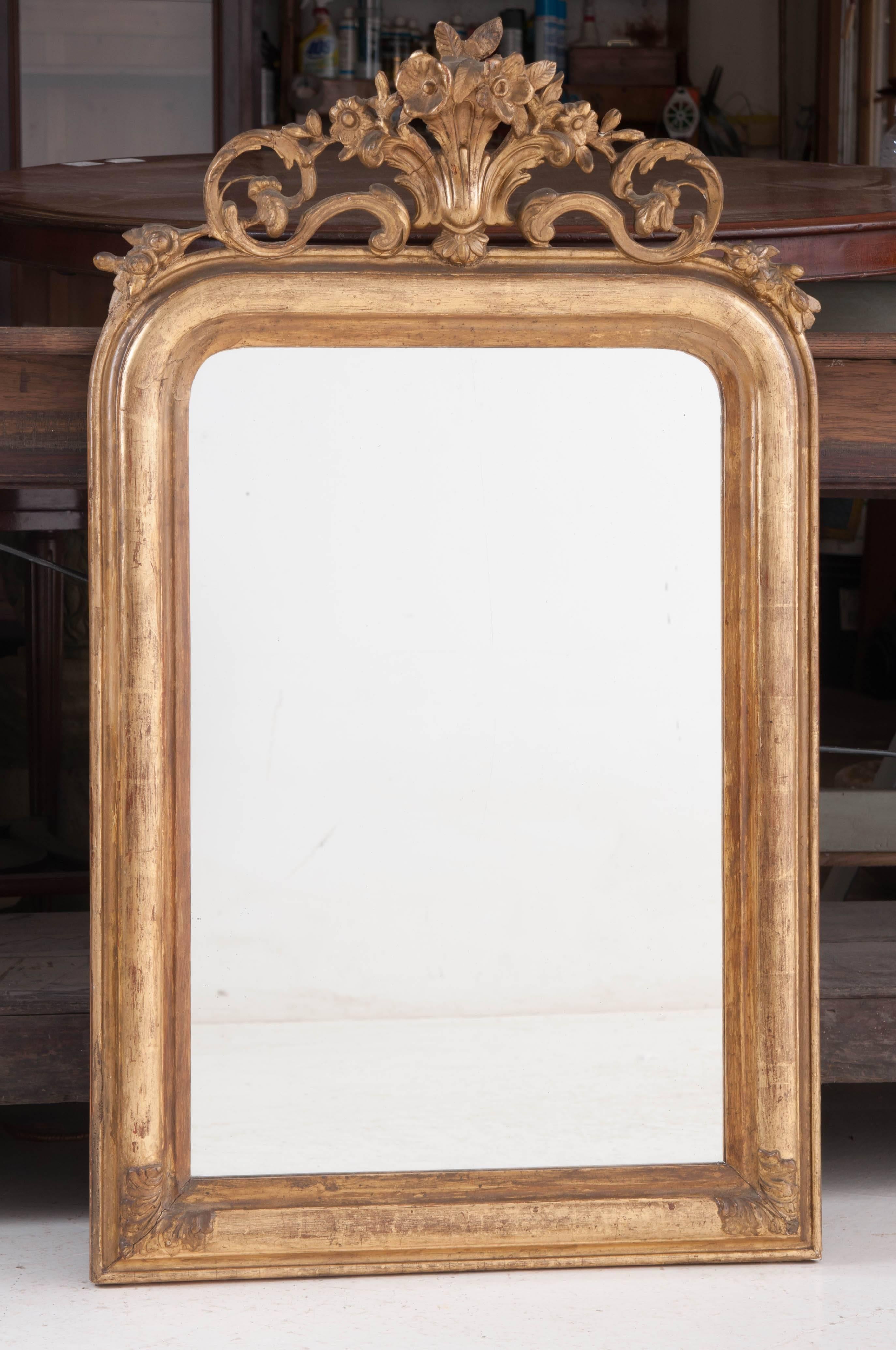 A fabulous gold gilt Louis Philippe mirror with decorative crest from 19th century France. The crest is composed of a floral bouquet that is supported by scrolled, ornate acanthus leaves. The gold gilt frame is free of ornamentation with the