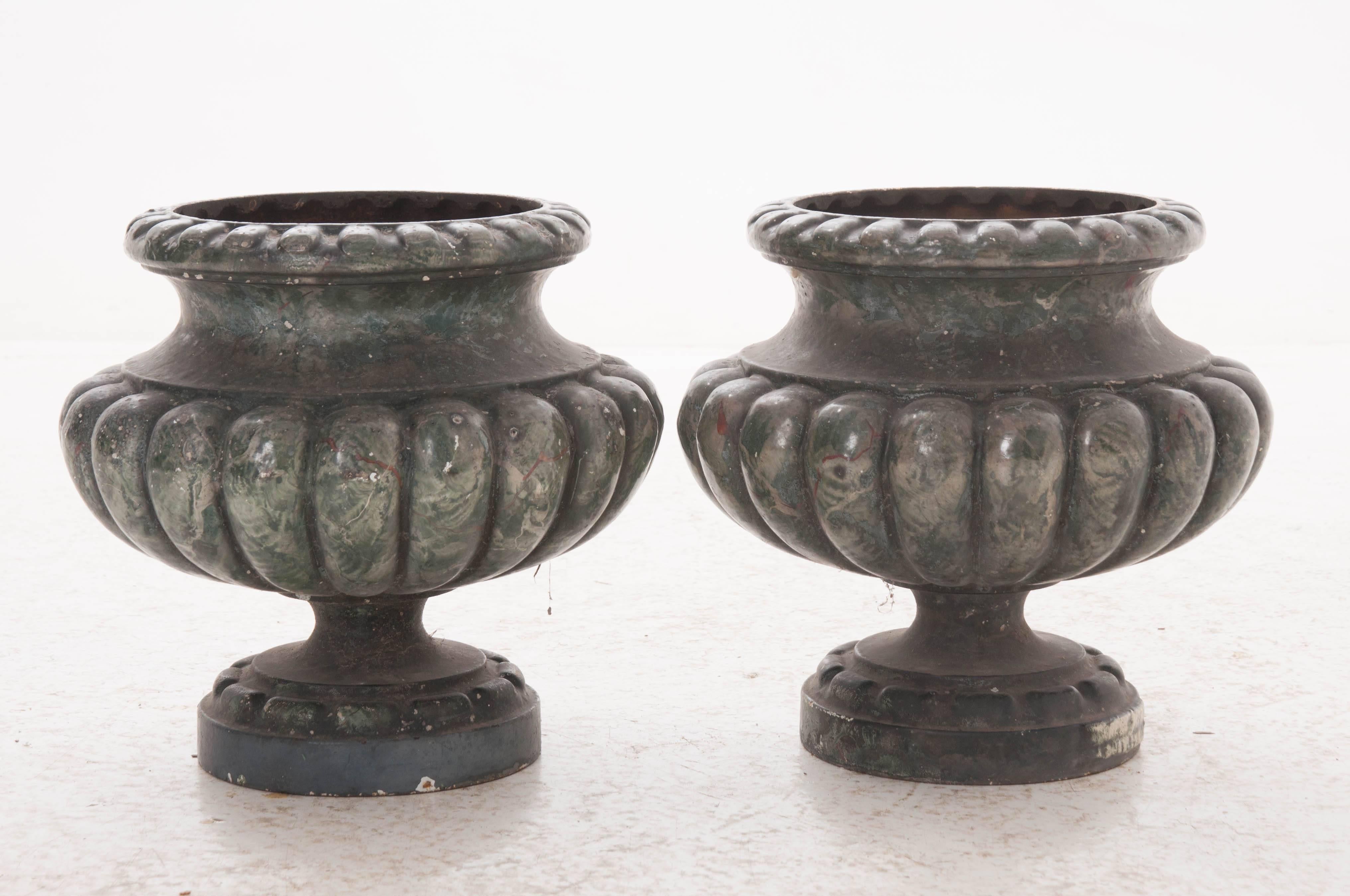 A fantastic pair of classical urn form, cast iron pots from early 20th century France. These pots have been painted in a realistic faux green and gray marble that makes these pots seem to have been carved from stone. These pots are both equipped