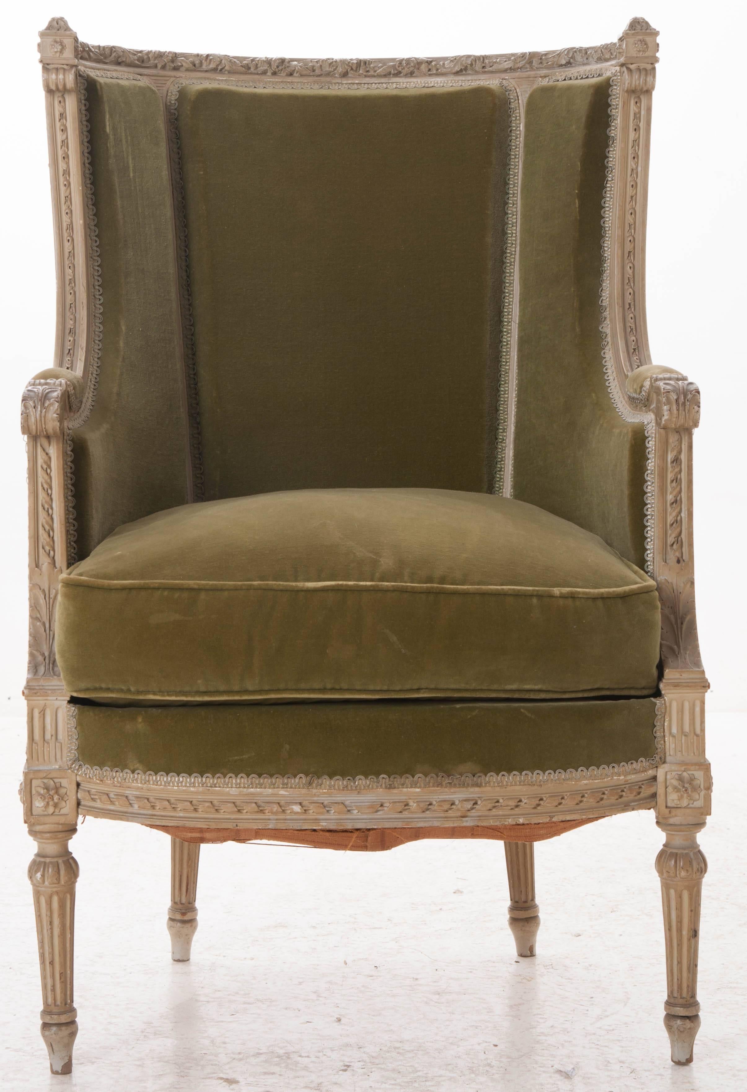 A masterfully carved 19th century Louis XVI painted bergère from France. Nearly every exposed surface of this chair's frame is embellished with fantastic detailed carvings. The top rail of this barrel backed piece is carved in a twisted garland