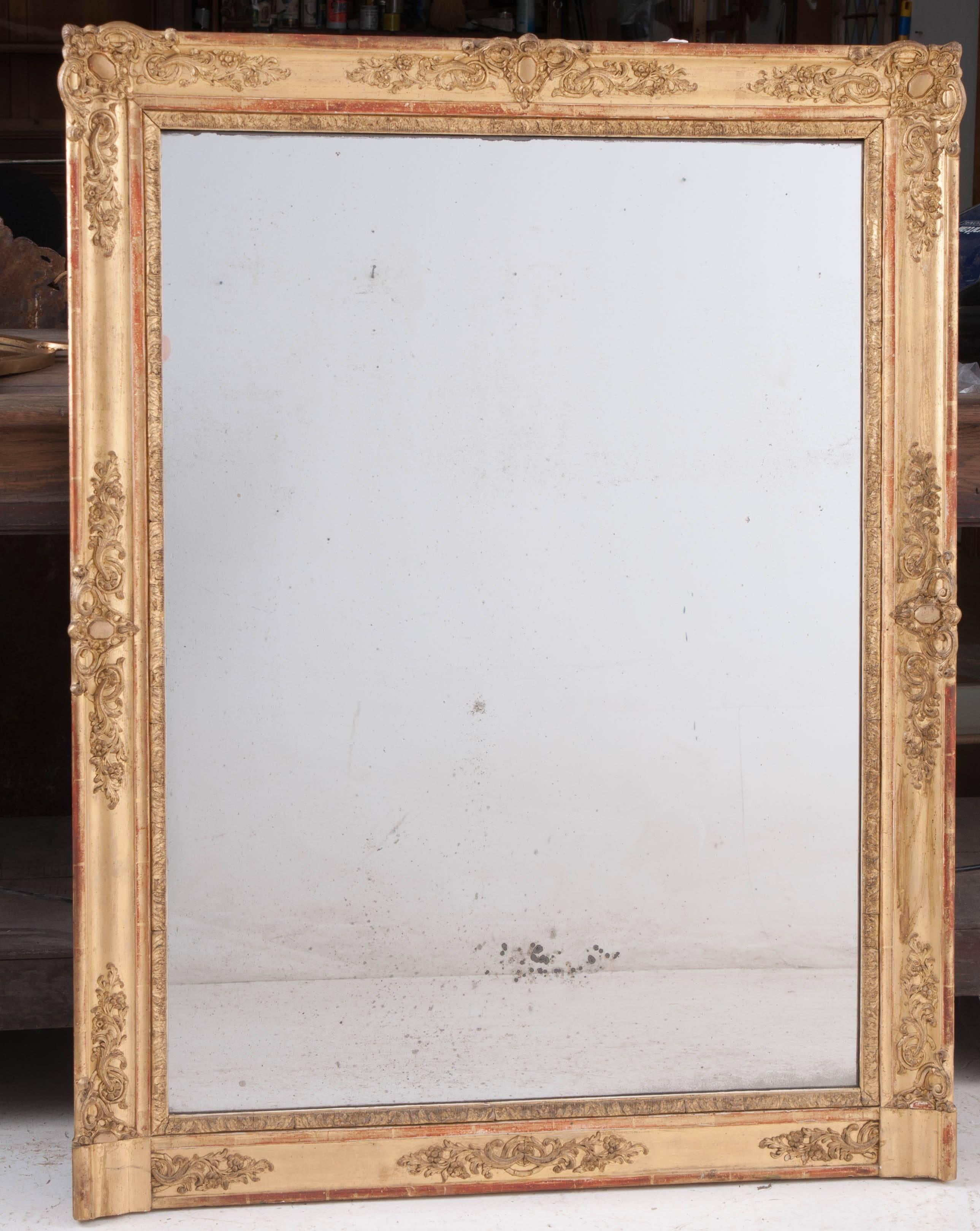 A grand gold gilt mantel mirror from 19th century, France. Decorated with symmetrically placed scrolled embellishments, the frame is ornate, yet restrained. The mirror has its original mercury glass that is wonderfully foxed. The gold gilt frame is