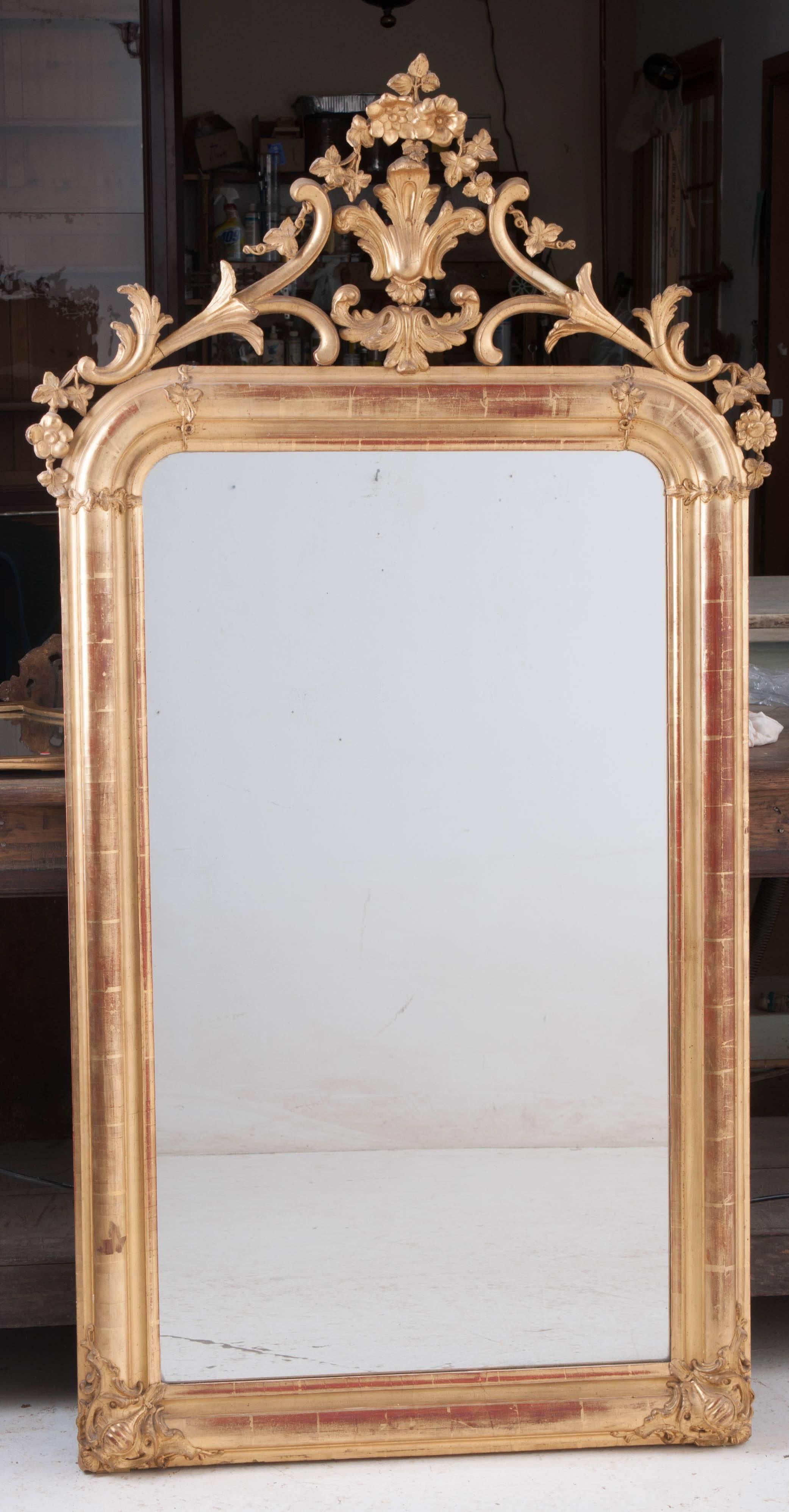 Blending elements of Louis Philippe and Louis XV, this beautiful gold gilt mirror comes from 19th century, France. A delicately carved crest crowns this spectacular mirror. The crest is composed of flowers, grapevines and tendrils and Classic