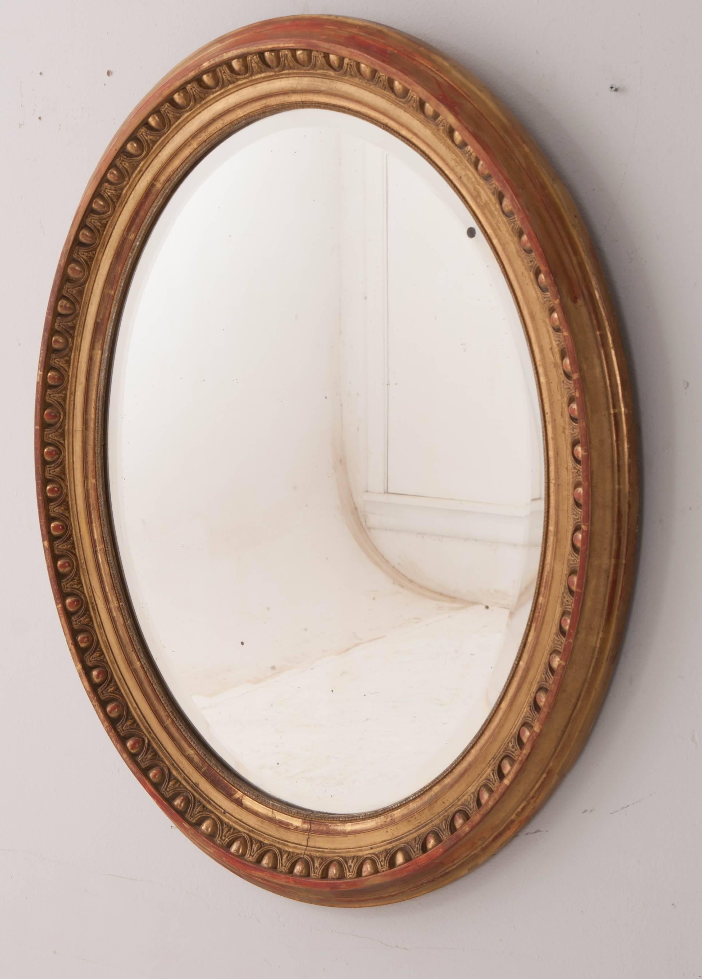 Spectacular patina overwhelms this gorgeous 19th century French oval mirror. The frame is embellished with an egg and dart motif that is finished in antique gold gilt that is stunning. Abundant French red warms the frame as it has become exposed