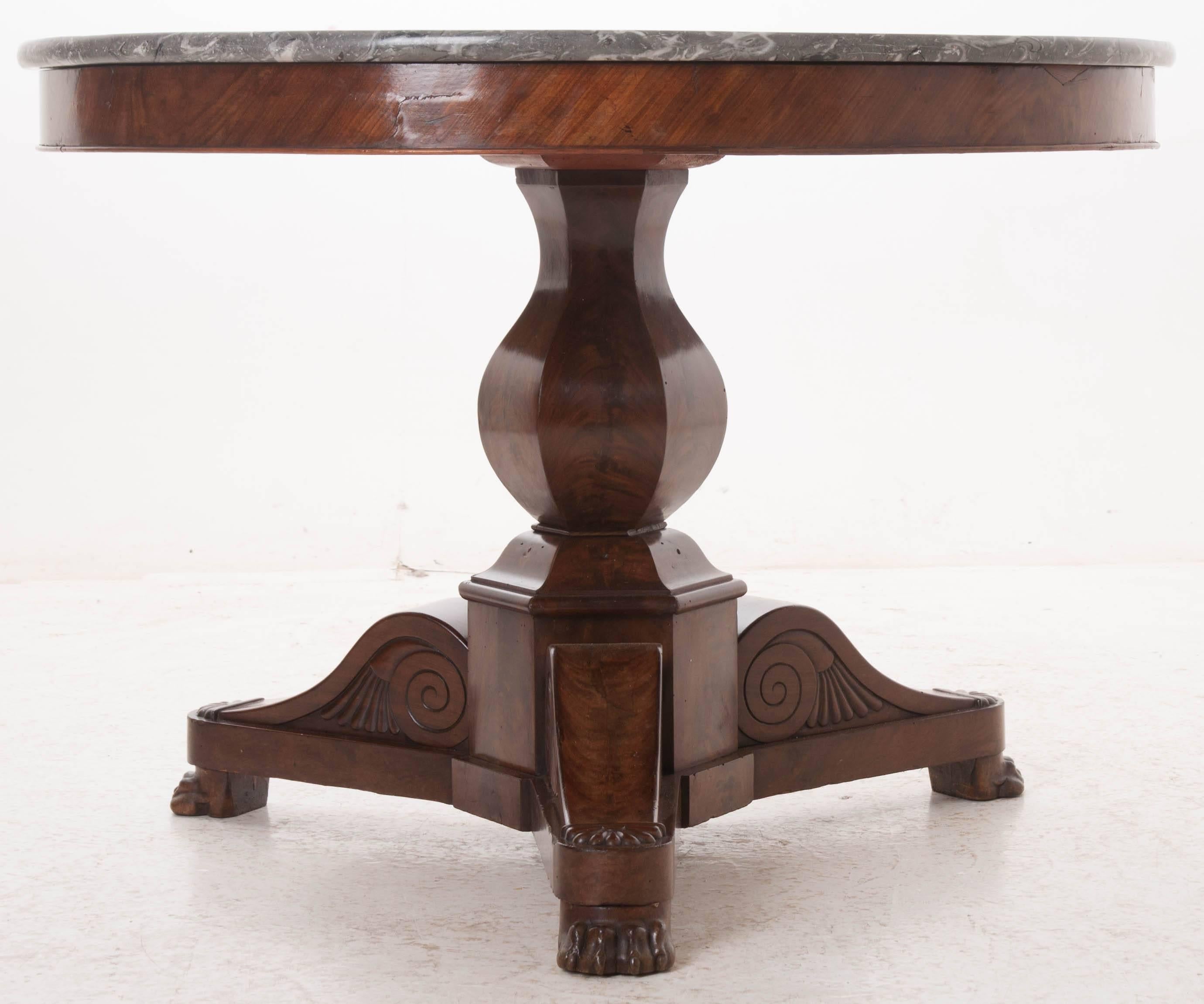 An outstanding French restauration mahogany center table with gray marble top. The marble top has a raised lip and is in excellent antique condition. The circular top rests on a mahogany tripod pedestal base with carved lion's paw feet. The base is