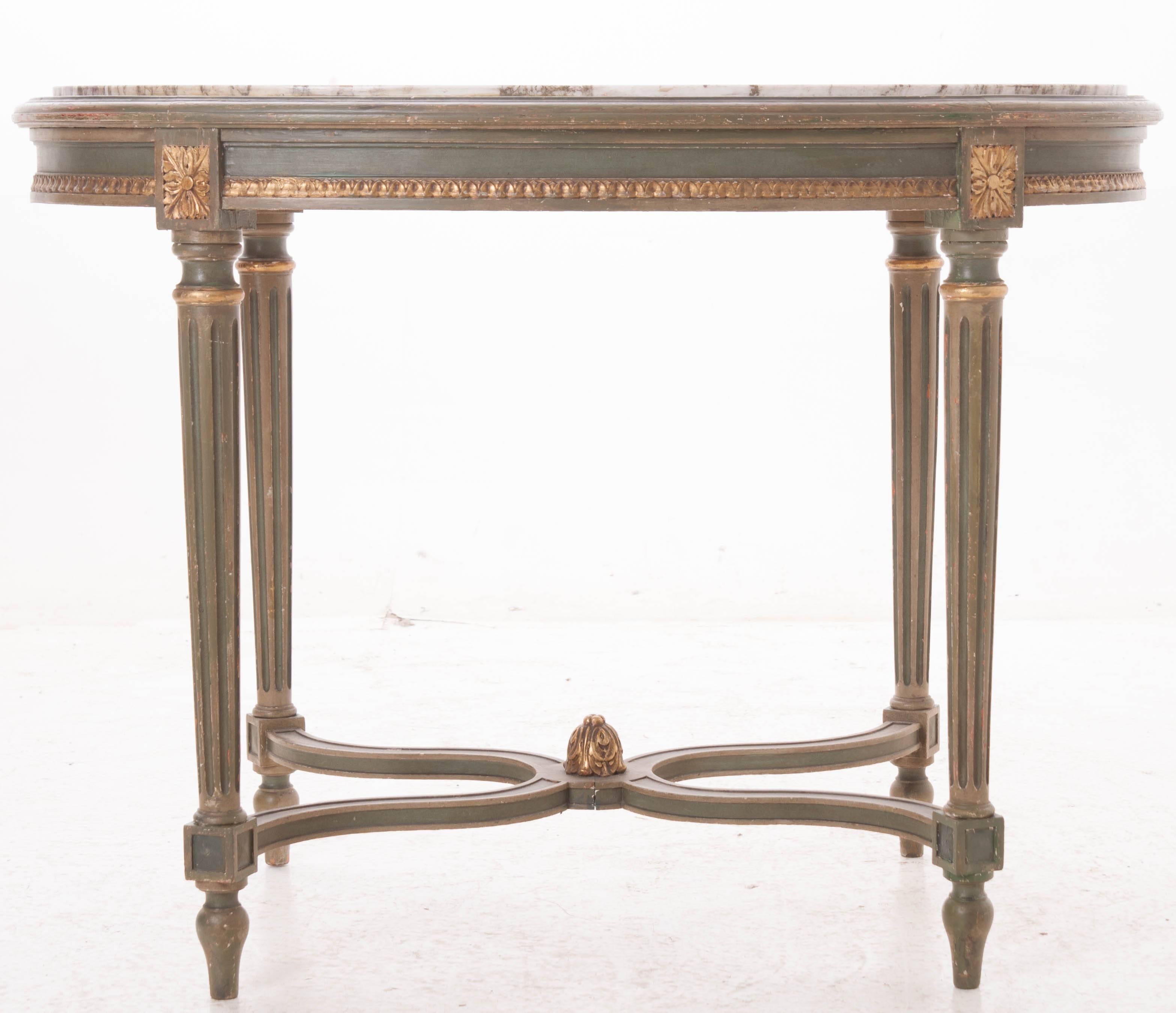 A stunning painted Louis XVI oval table with marble top. The marble top is exquisite. It is set into the table but is still removable and has beautiful veins of gray and violet running throughout. Gold gilt trim accents can be found in the apron,