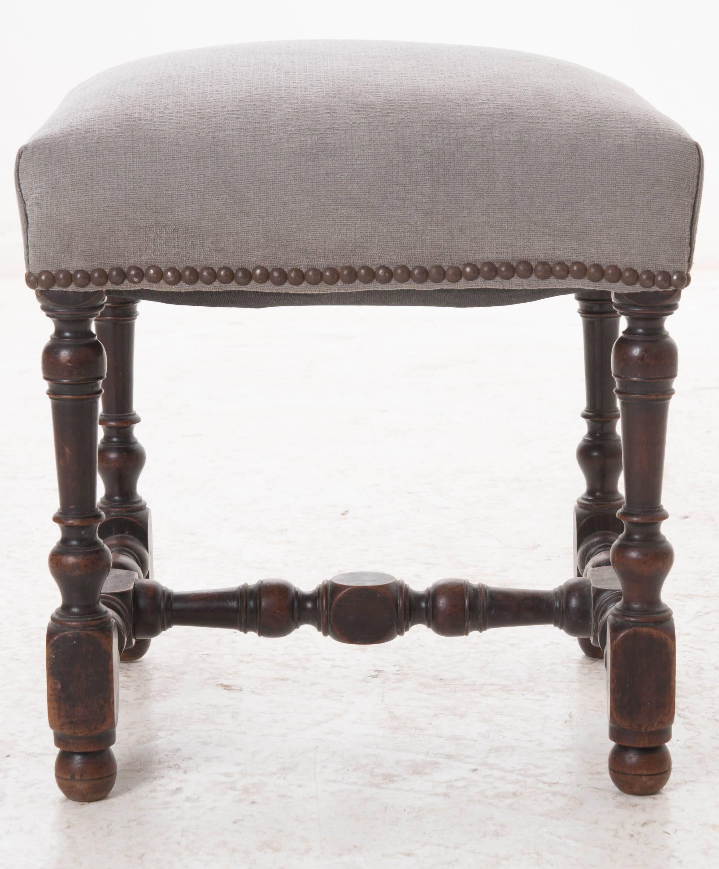 A charming, newly upholstered stool with nailhead trim from 19th century, France. Marvelously turned mahogany legs are joined by an equally marvelous turned stretcher. A perfect little place to rest your feet at the end of a long day!