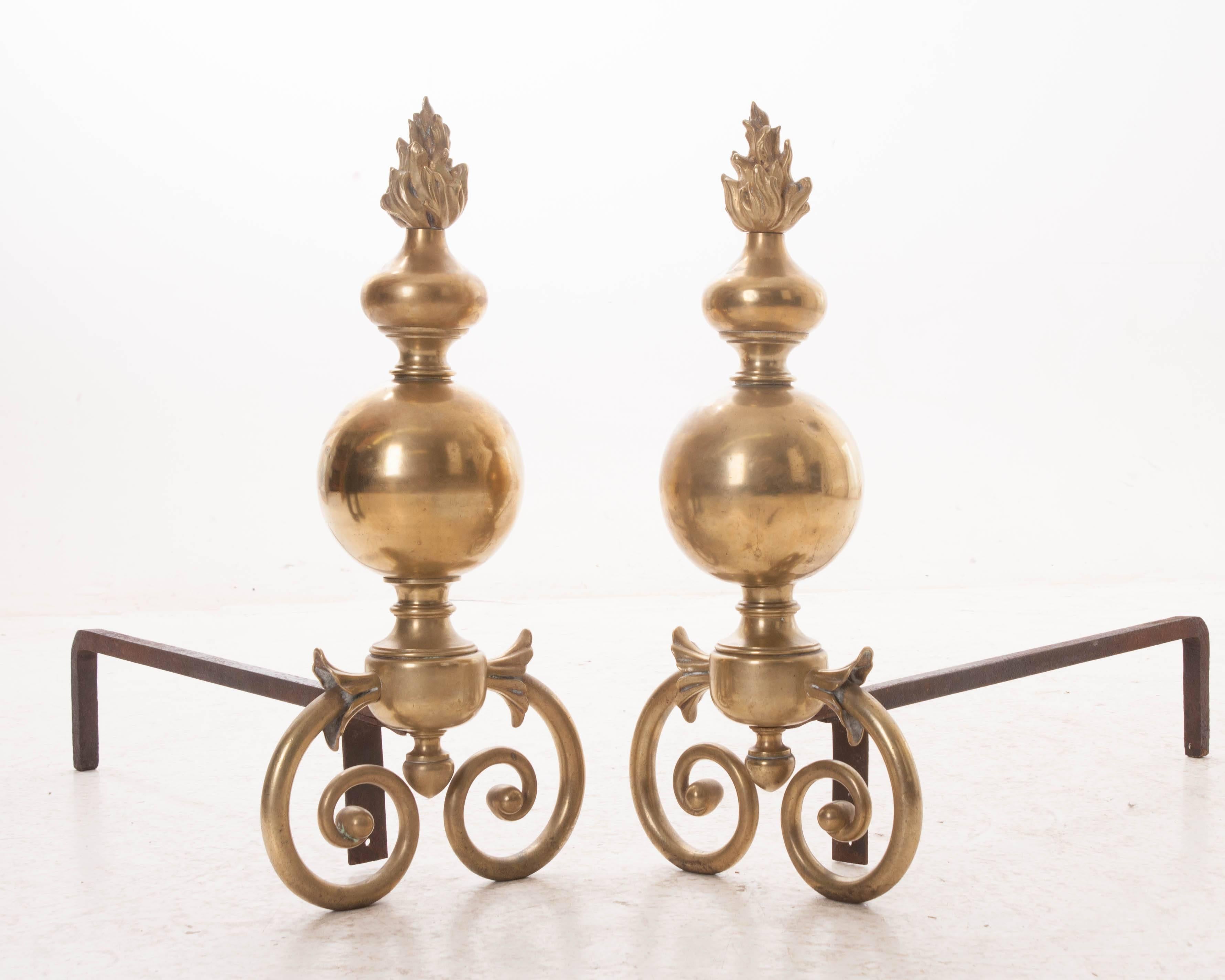 A striking pair of large-scale French 18th century Louis XIV brass andirons. Crowned with flickering flame finials, these larger than life andirons are not only bold and commanding, but beautiful and majestic. A nearly 250 year life span has
