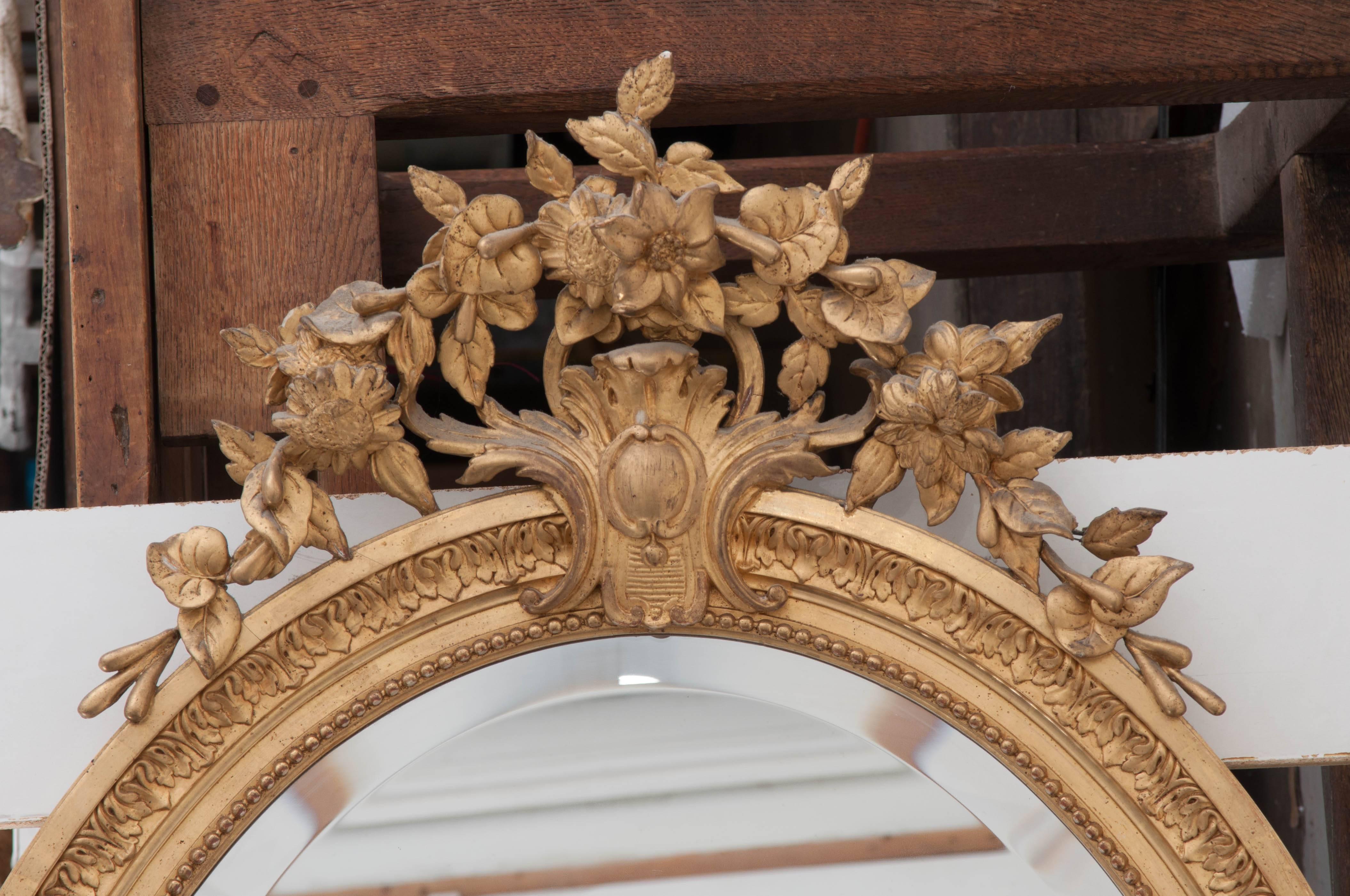 Fanciful and fun, this 19th century French oval gold gilt mirror boasts intricate, carved details from top to bottom. A carved garland of flowering vines crowns the brilliant mirror, with cartouches of flowing acanthus leaves at the top, bottom, and