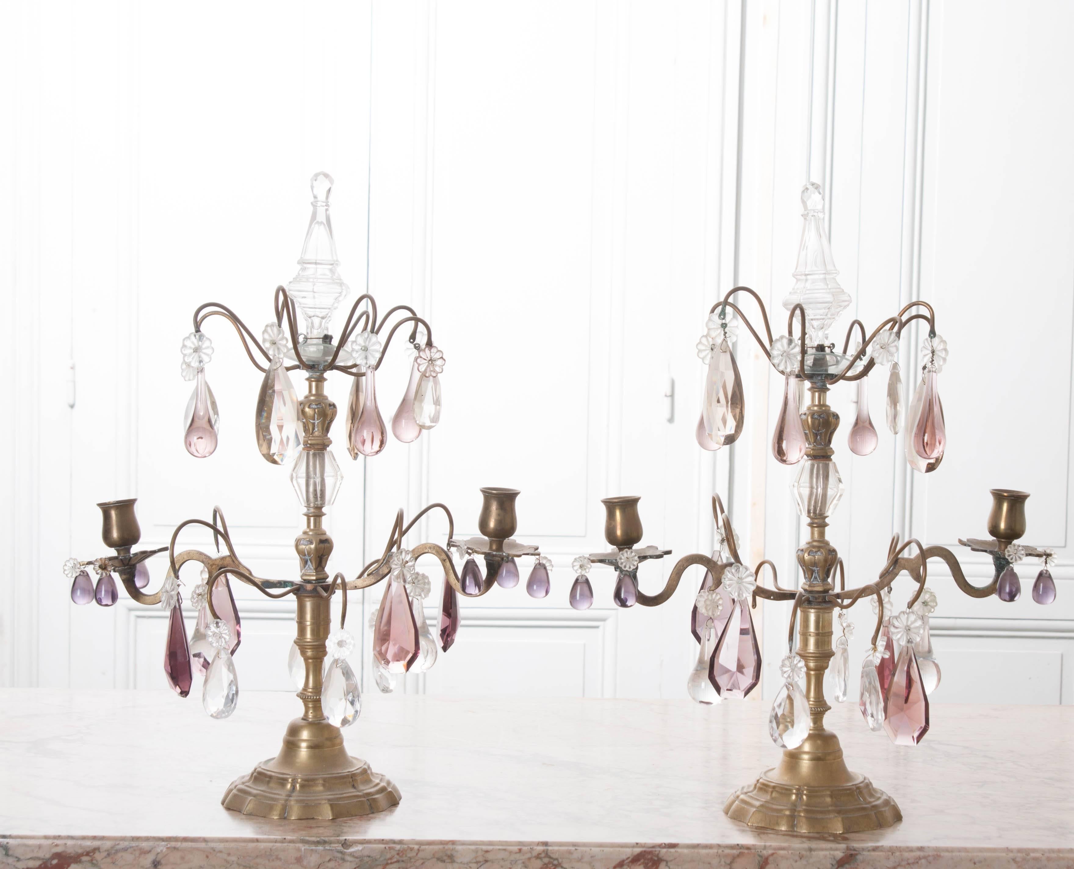 This gorgeous pair of petite brass and crystal candelabra girandoles were masterfully crafted in 19th century, France. Each girandole has two arms, each of which holds a single candle. Beautiful colored crystals drip from the brass bobeches and