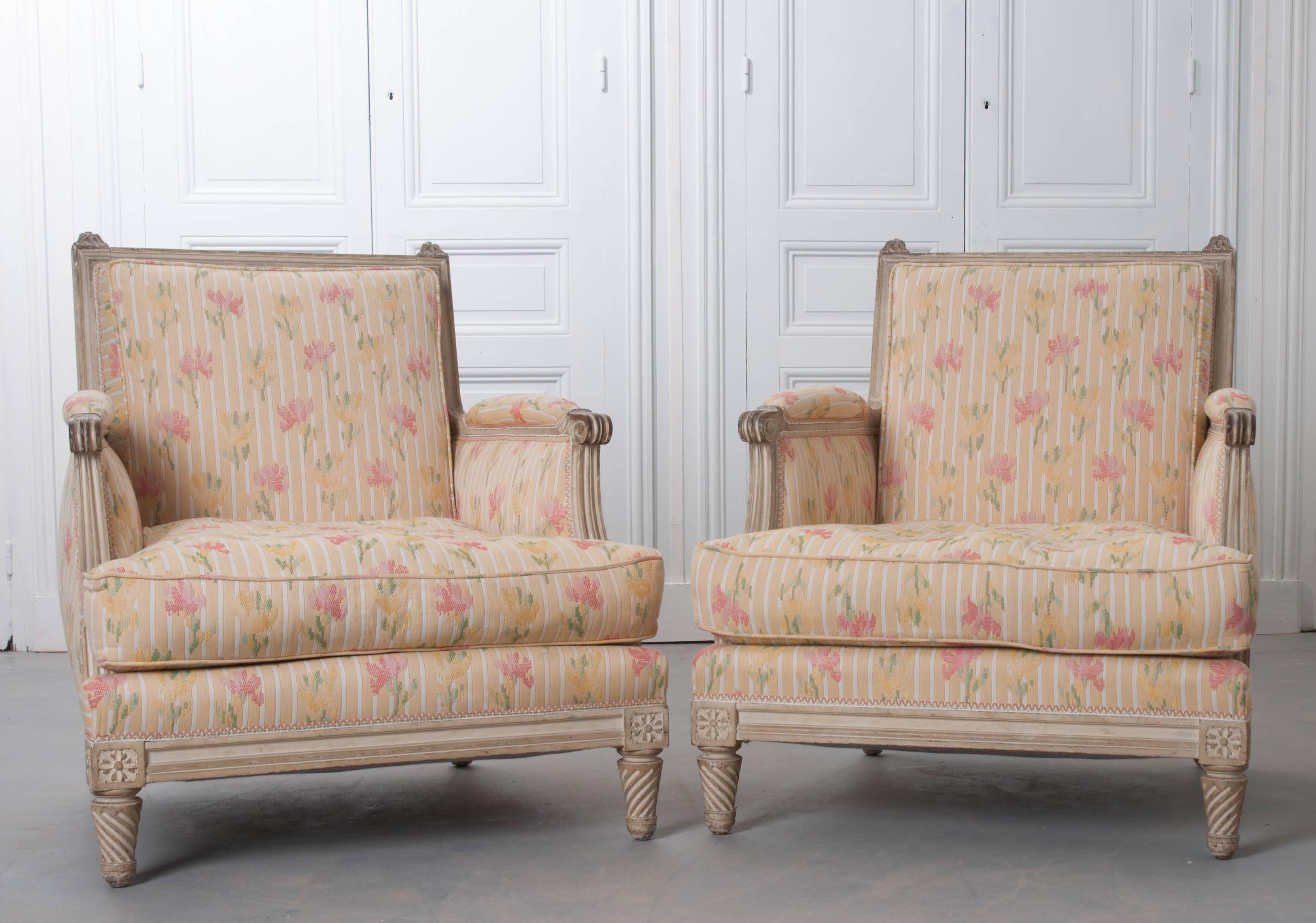 A lovely pair of French painted bergères with square backs made in the 19th century. The original paint is aged with wear and life experience. The pair of chairs sit low with squat, spiral carved feet lifting it from the ground. The frame is sturdy