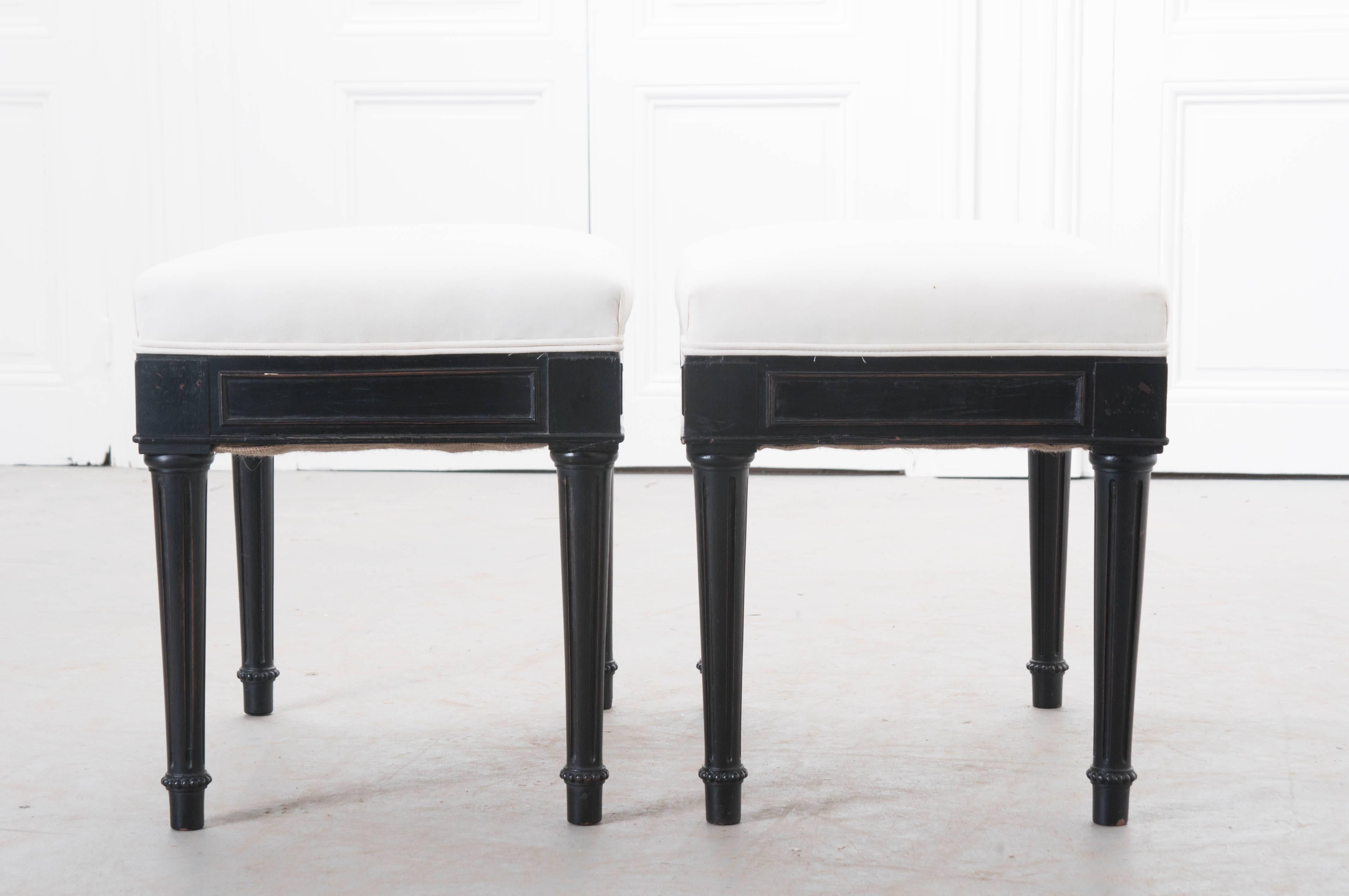 Two handsome ebony stools that have newly upholstered seats from early 20th century England. These beautiful antique stools' subdued design is tasteful and timeless, and the ebony finish has acquired a wonderful patina through the years. Each stool
