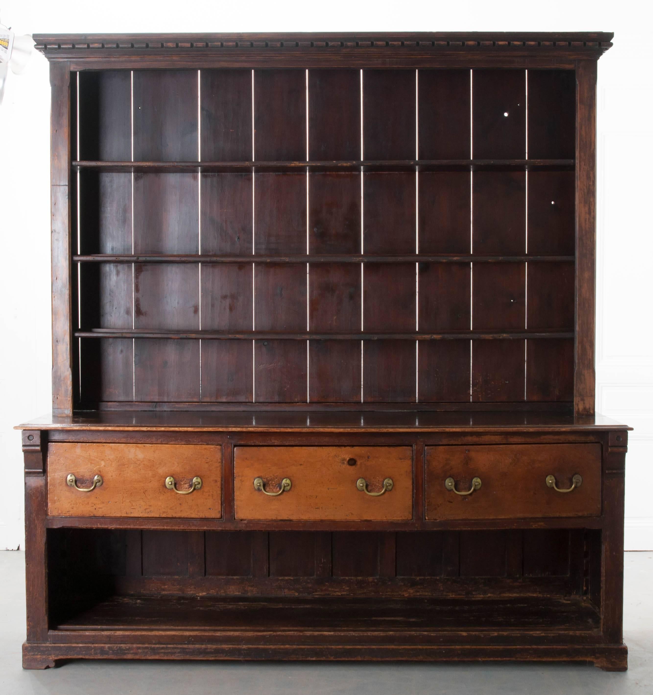 A commanding pine dresser with pot board from the early part of the 19th century, England. Display your china and decorative objects on one of the three adjustable shelves. The molded cornice features a dentil motif with rounded edges. The dark pine