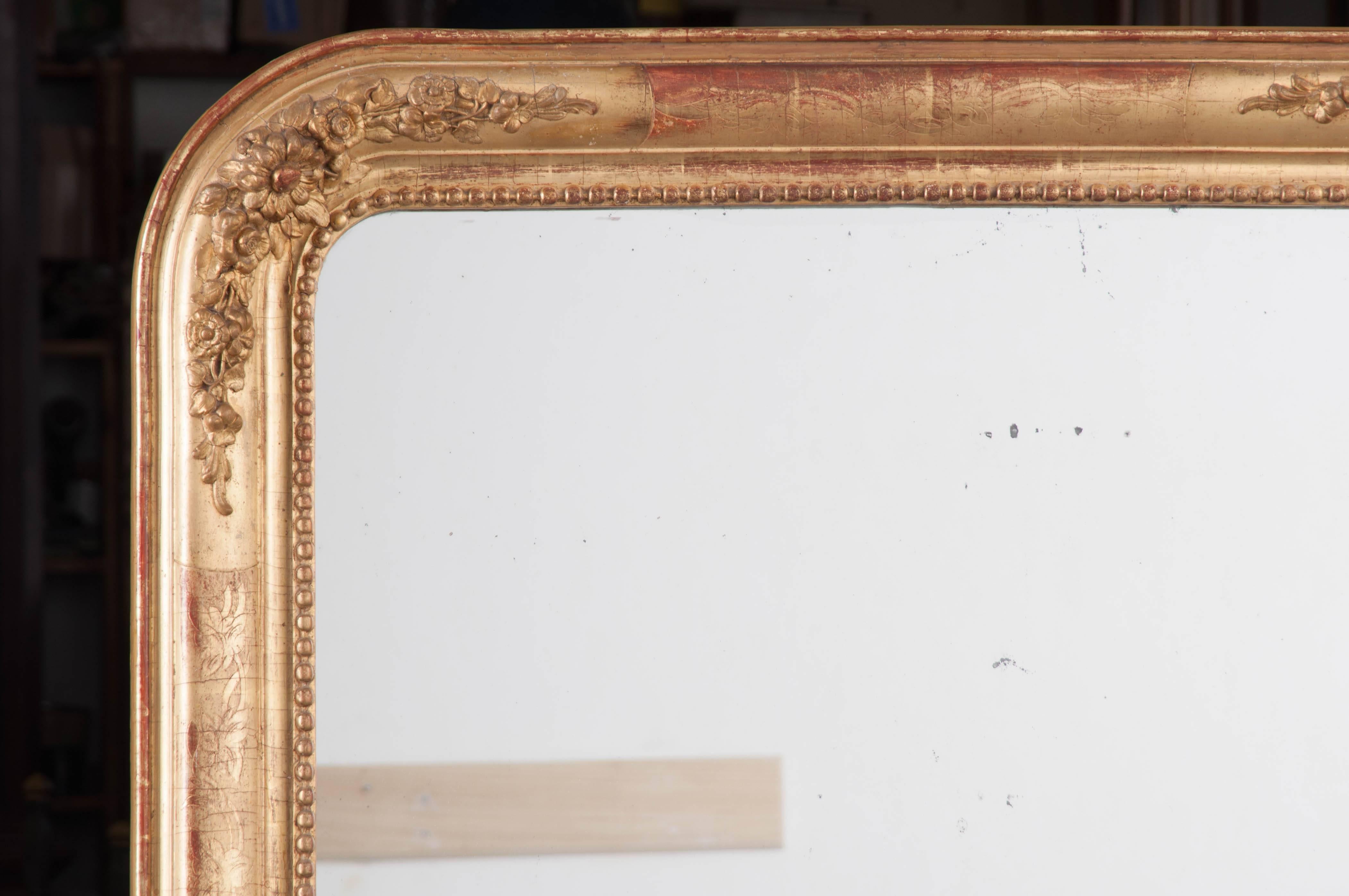 A lovely Louis Philippe gold gilt mirror with pleasant floral ornamentation from 19th century, France. The frame has aged gracefully, with its red bole substratum becoming exposed after decades of feather dustings. The mirror's corners are