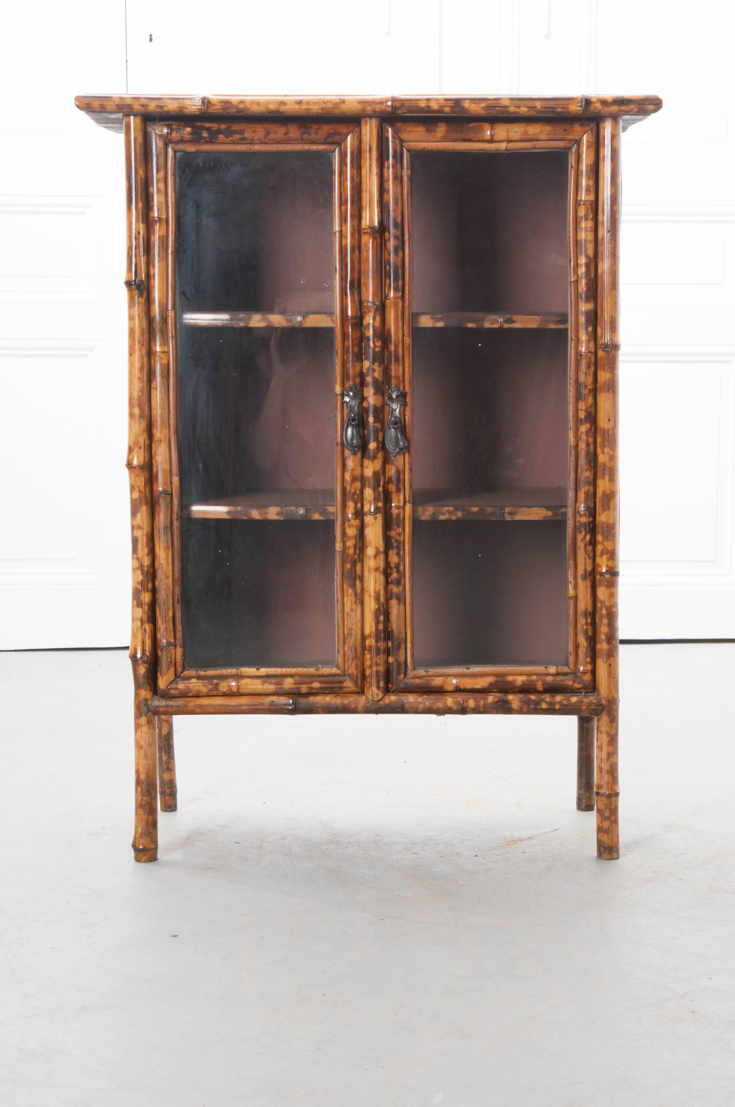 A wonderful 19th century English bamboo bookcase with glass doors and fantastic stamped leather sides. The top is accented with an Asian painted scene depicting mountains, cherry trees in bloom, and a distant pagoda. The two glass front doors close