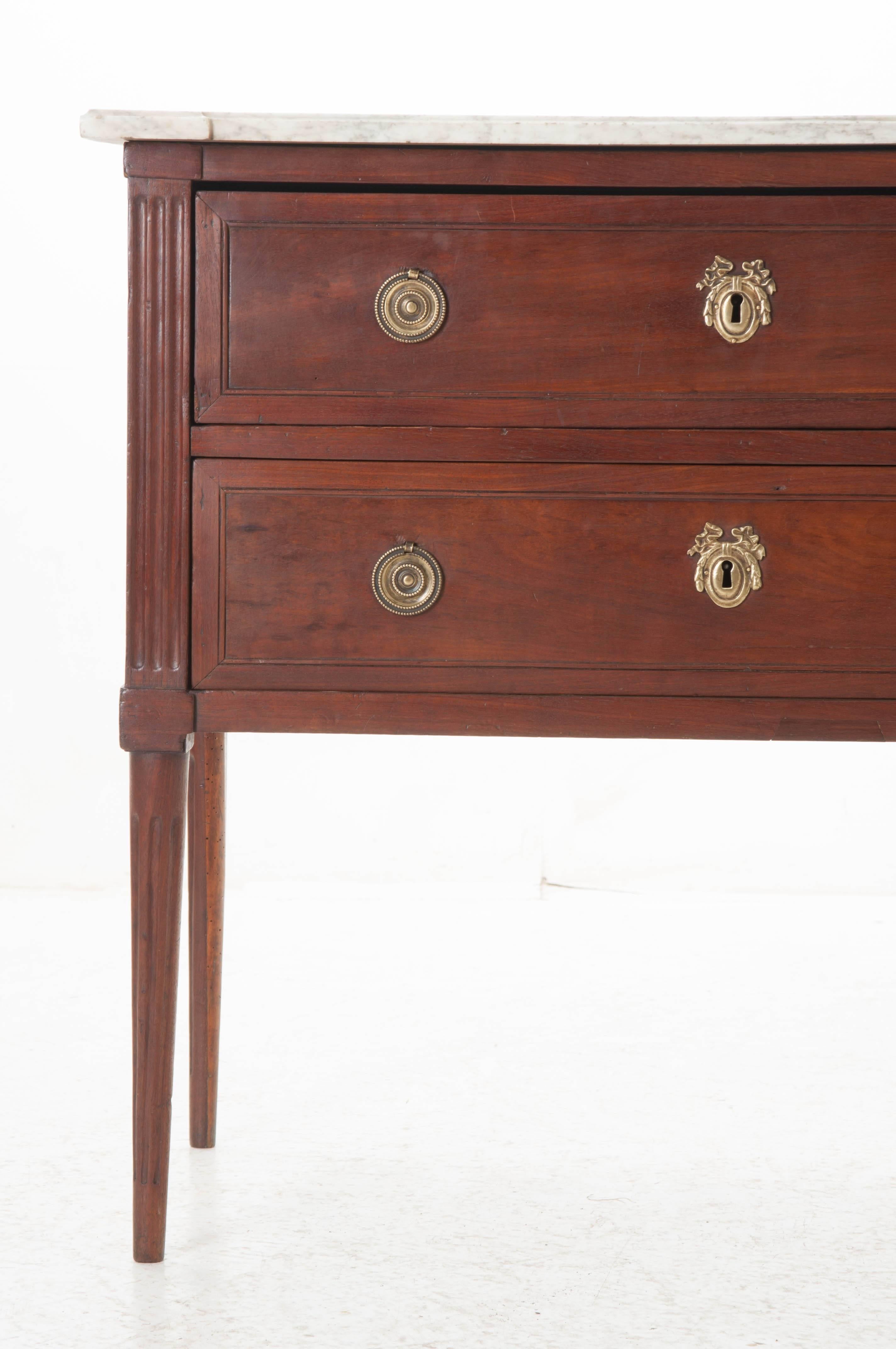 Louis XVI style mahogany two-drawer commode. Original shaped marble top is in antique condition with minimal discoloration. The pilaster corners are fluted and the whole piece is supported by tall tapered legs. The drawers are equipped with