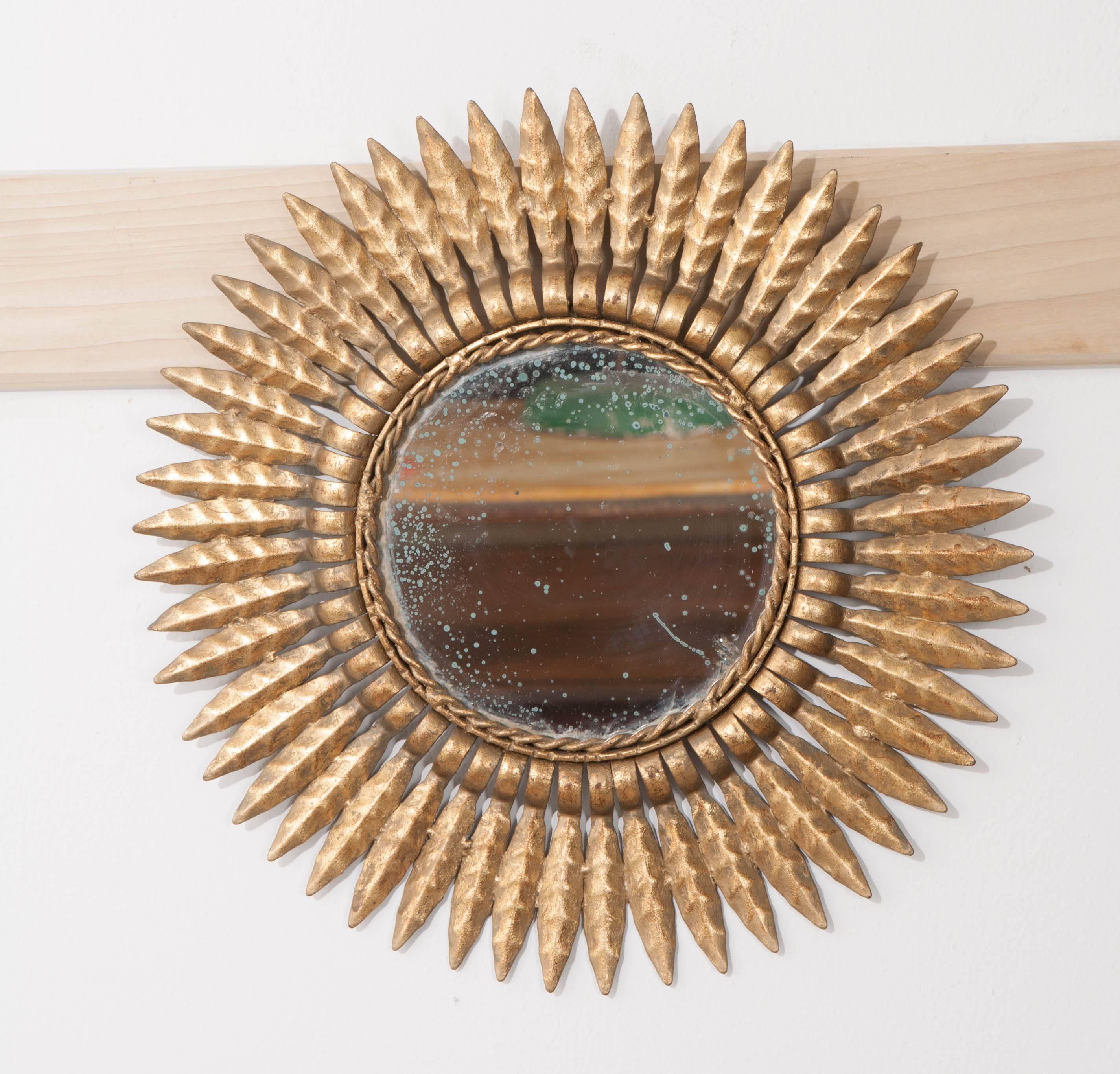 A lustrous French gold sunburst mirror, made of metal, at the beginning of the 20th century, France. The mirror has its original mercury glass, which has aged wonderfully. The mirror is secured to its frame with twisted metal trim. The piece's