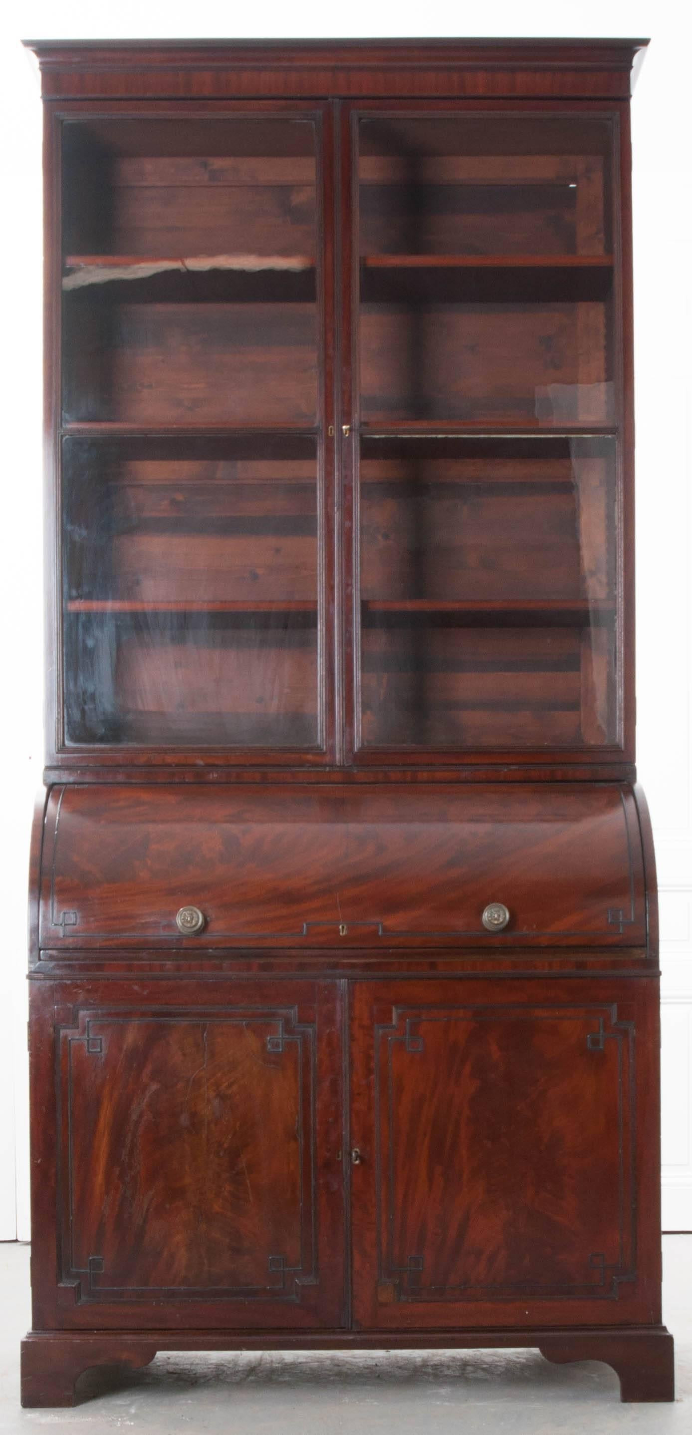 A handsome mahogany secretary with glass-front cabinet and roll top from England, circa 1830. This tall secretary has an upper body that is equipped with three finished and adjustable shelves that are visible behind two lockable doors, which retain