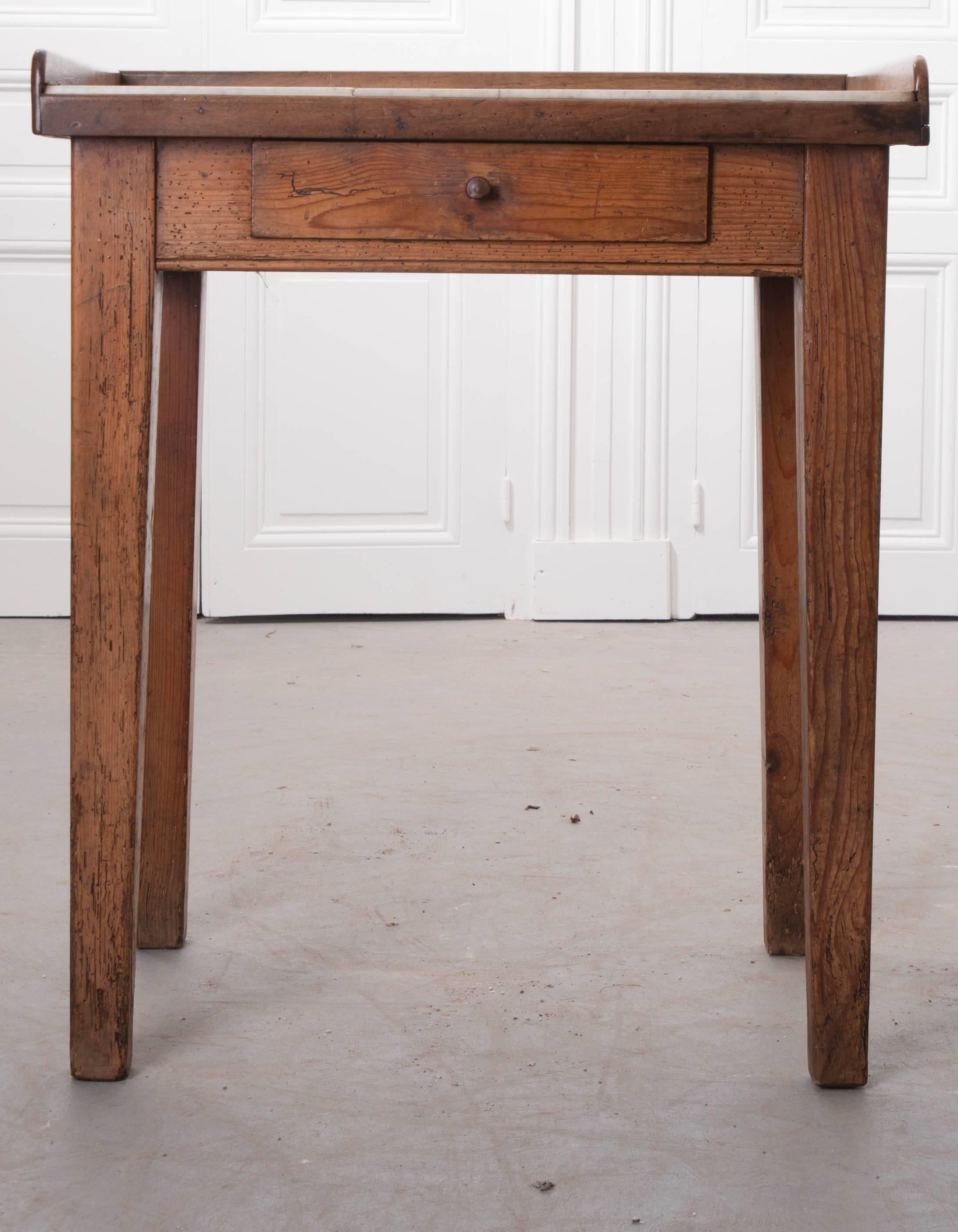 A 19th century butcher's table, made of pine, from England. This table has its original marble top, which is worn and aged, with an old crack and fracture that gives the butcher's table a matured appearance from a lifetime of use. The marble top is