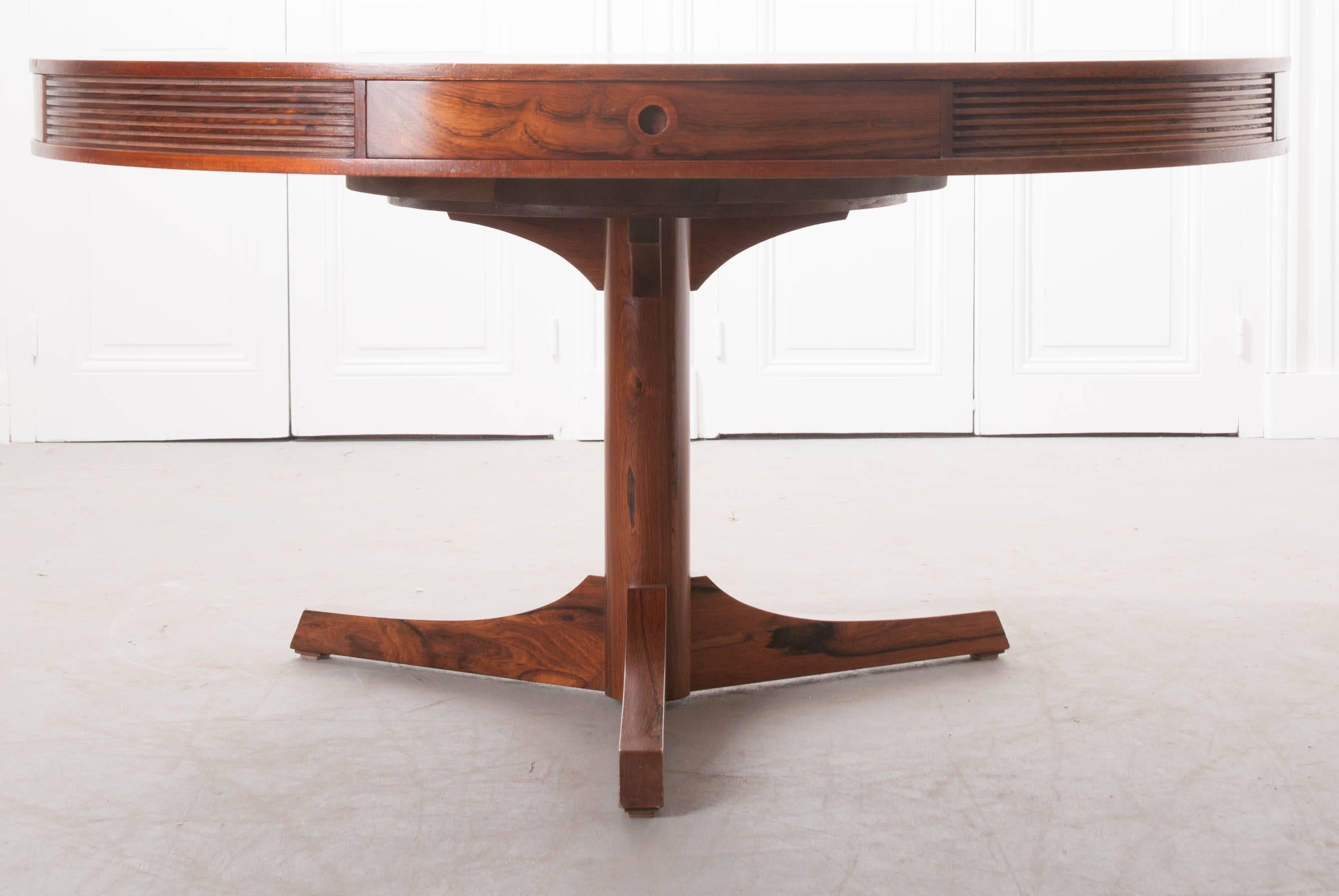 A stylish round dining table, made in England, in the early 1960s. This remarkable piece is made of Brazilian rosewood, which has stunning grain and rich, vivid color. The reeded apron contains four drawers with curved fronts and round, recessed