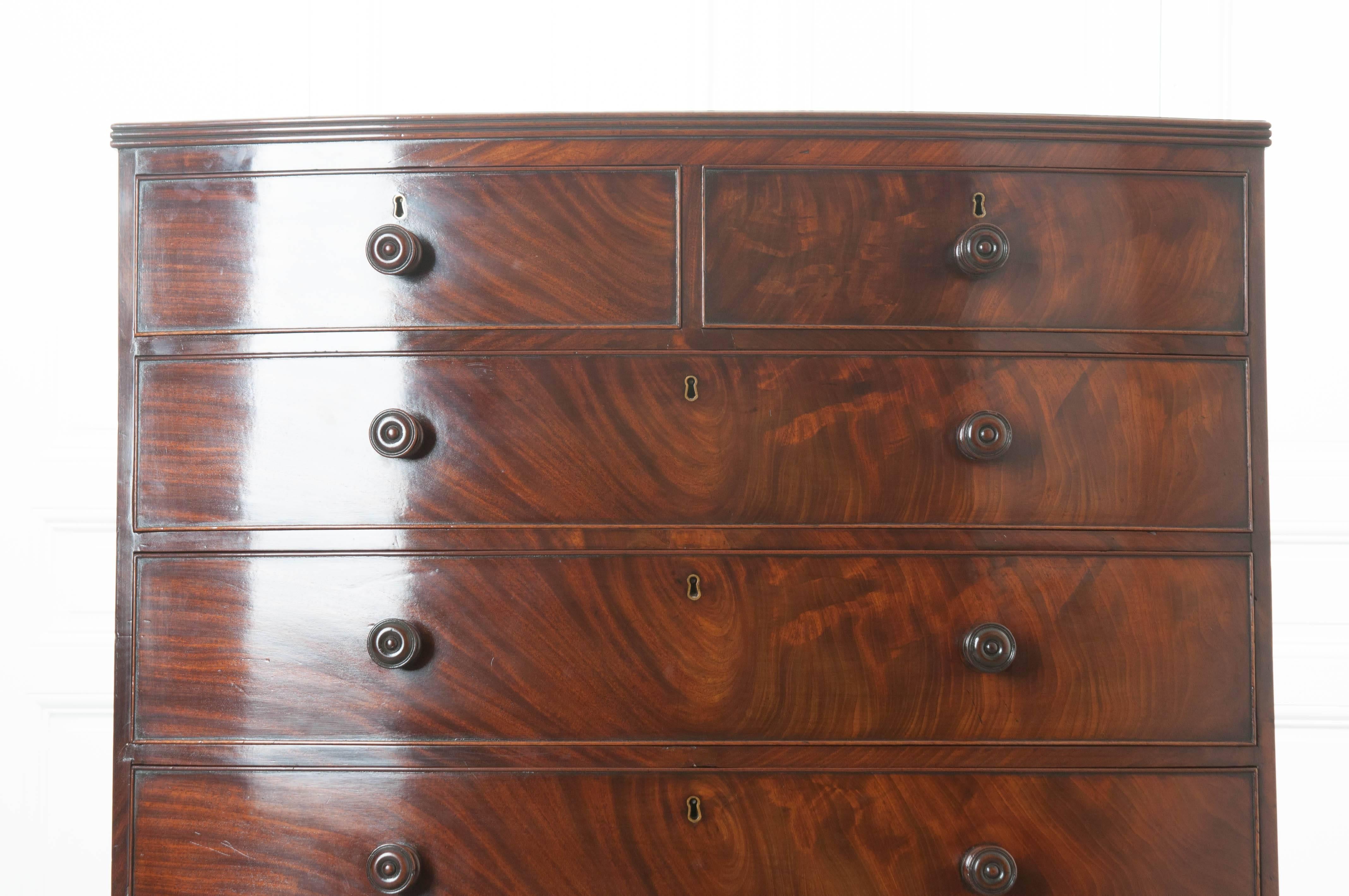 A stately, tall English mahogany chest of drawers from the 19th century. This exceptional chest is complete with six graduated drawers, all furnished with turned wood knobs and inset brass escutcheons. The bowed façade is finished in stunningly