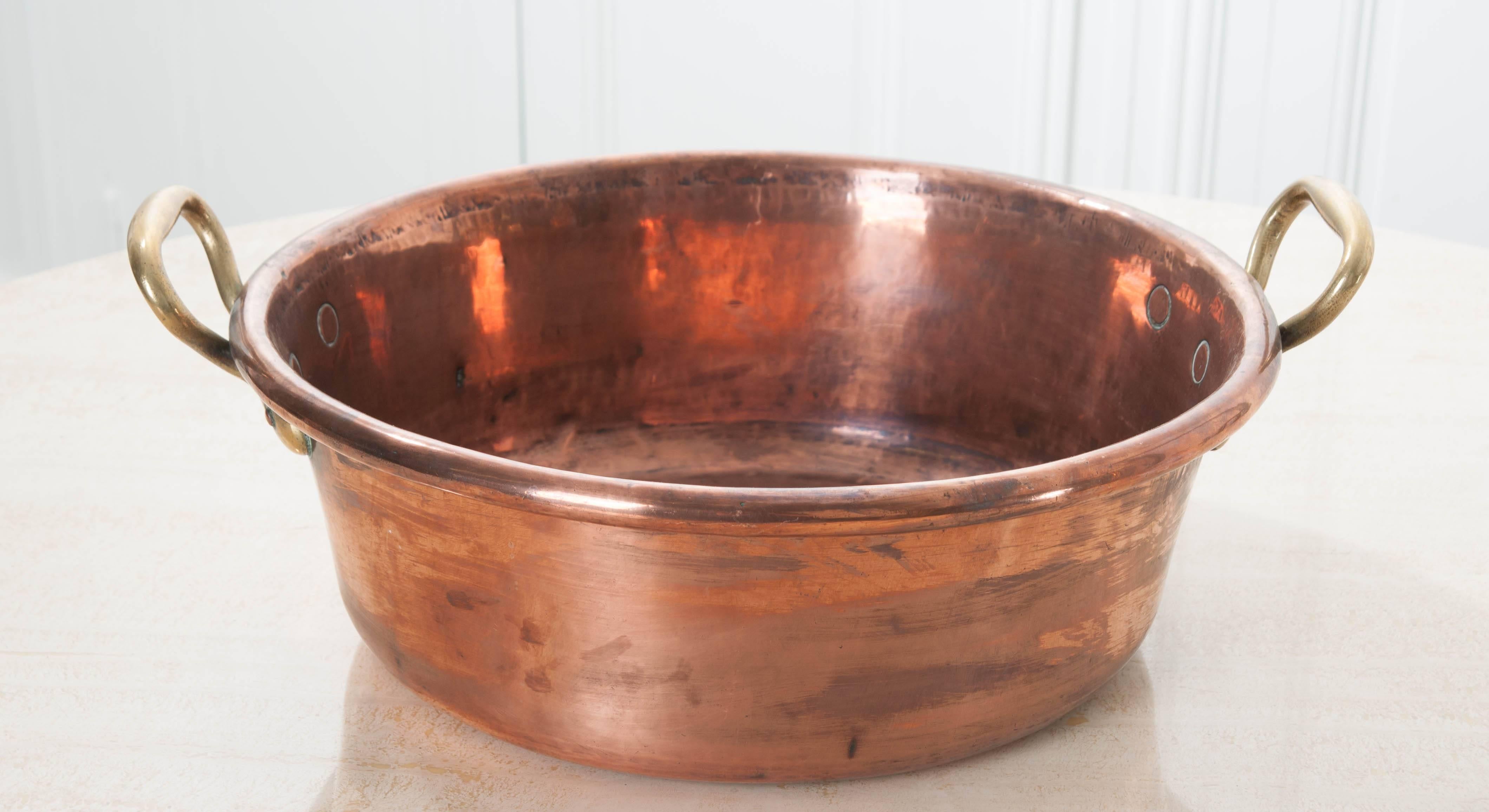 A beautiful, large copper cauldron with brass handles from the early part of the 20th century. The cauldron gleams, as the recently polished copper reflects light beautifully, creating a metallic luster that is warm and pleasant. Two brass loops
