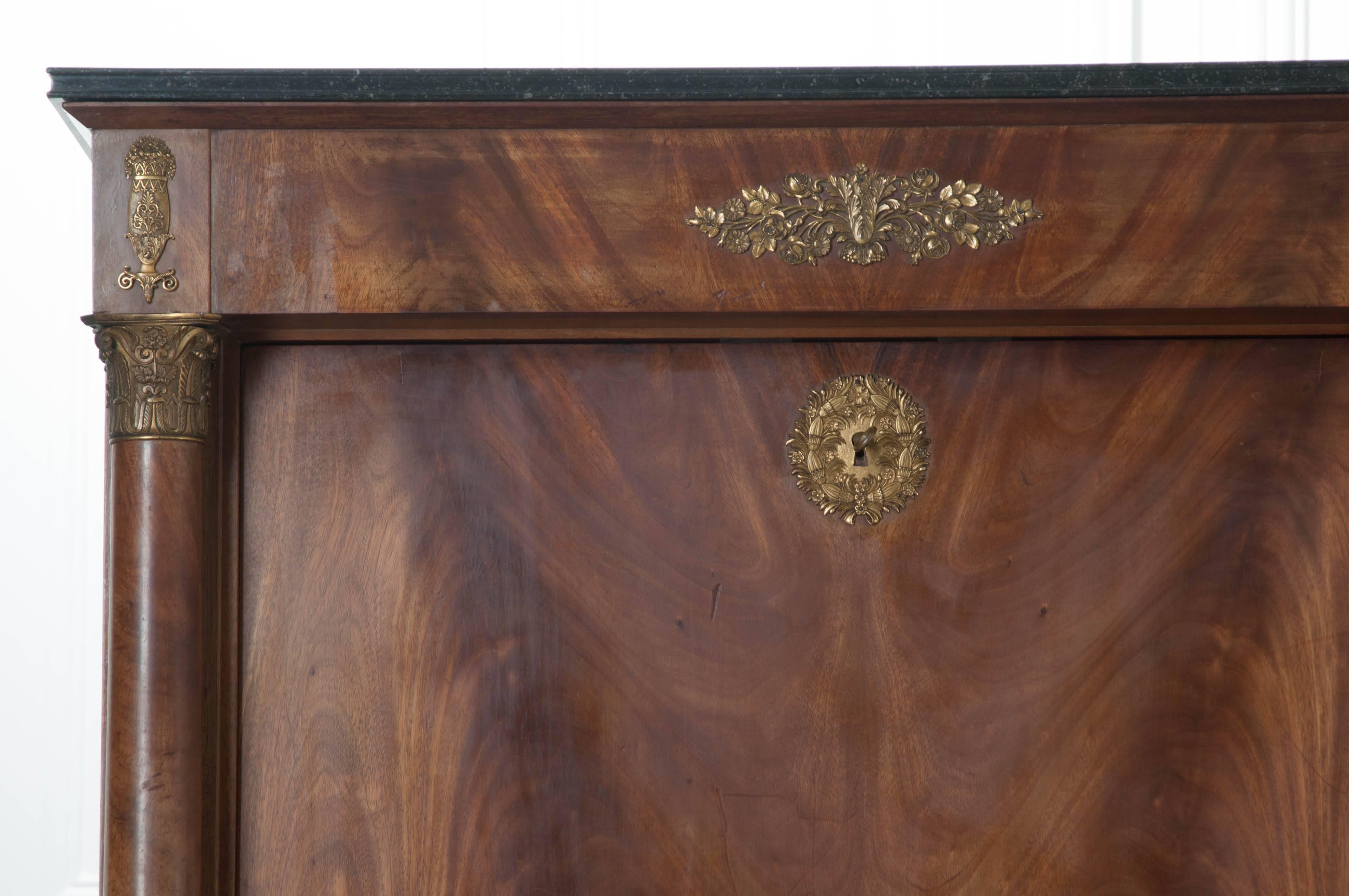 A stunning 19th century Empire secretary, in mahogany, from France. The desk has a black, fossil marble top with finished edge, that is in spectacular antique condition. The front of the desk folds forward to reveal the piece's work area. This space