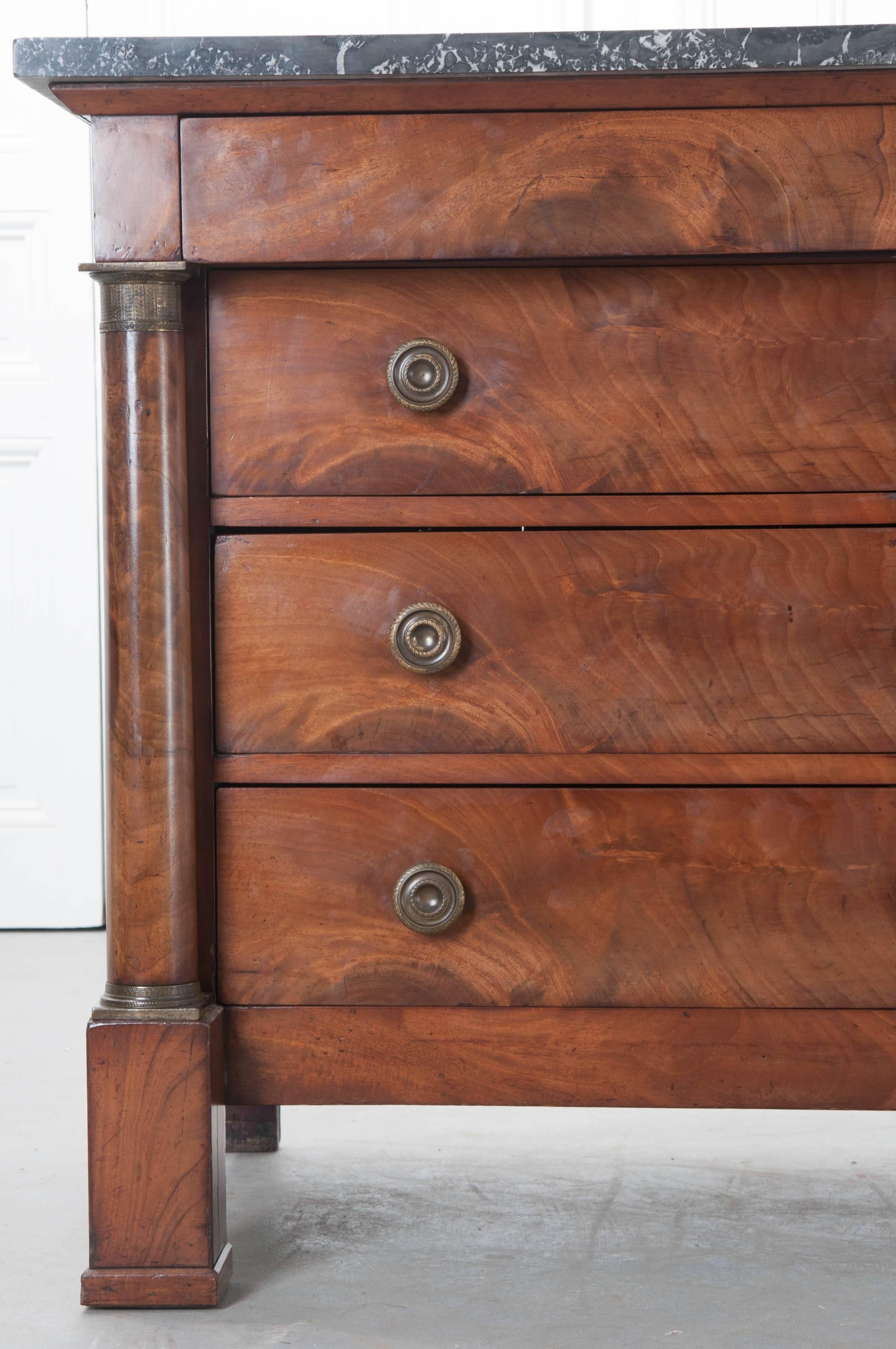 Extraordinary bookmatched walnut veneer graces this gorgeous Empire period commode from France. The piece has a slate colored marble top, with white veins, that is in excellent antique condition. The commode is complete with four drawers, the