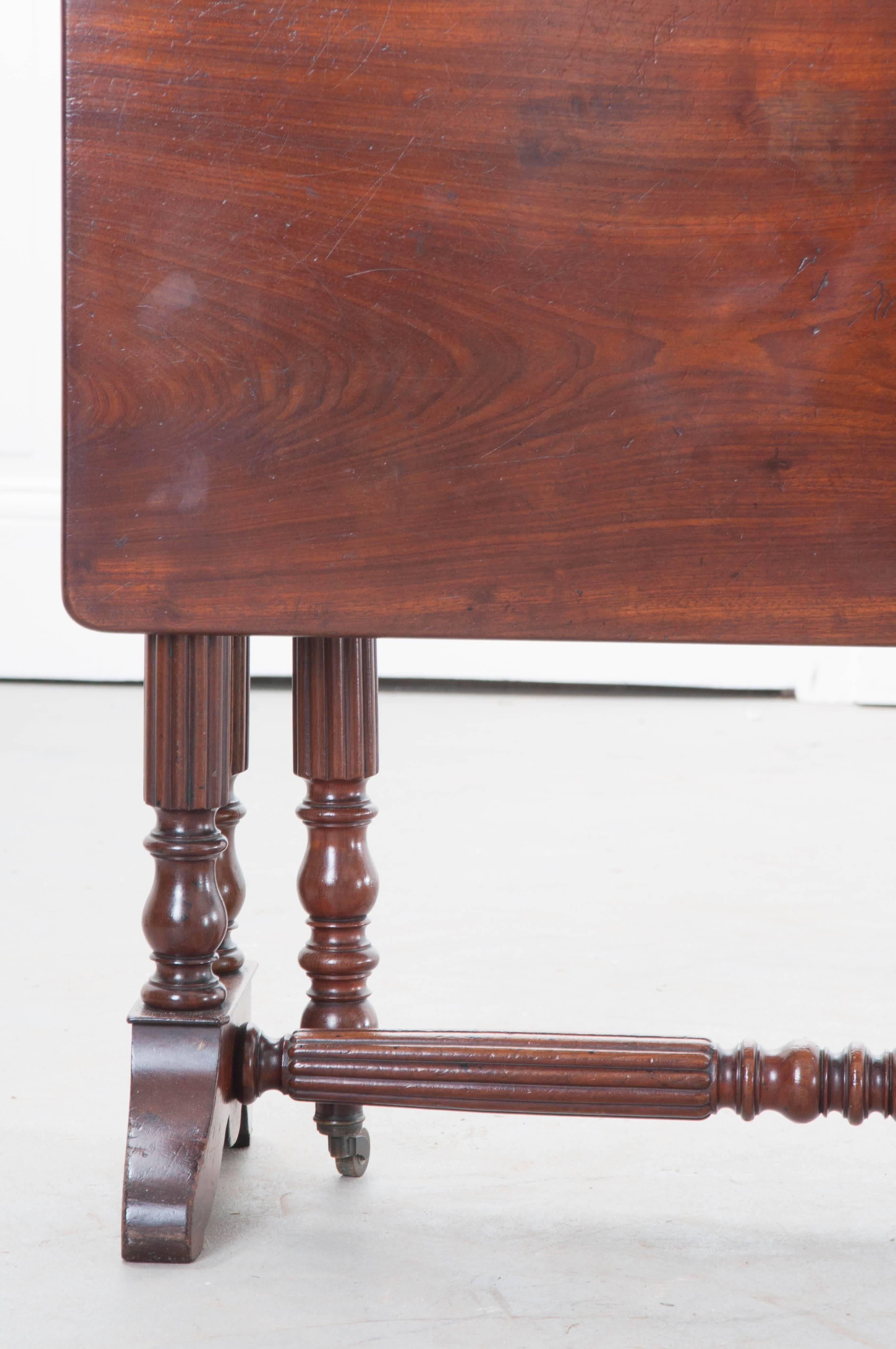 Rich mahogany was chosen to construct this handsome Regency drop-leaf table from 19th century, England. The table has beautifully styled legs that have been turned and finished with a reeded motif. The two legs that swing to support the top, when