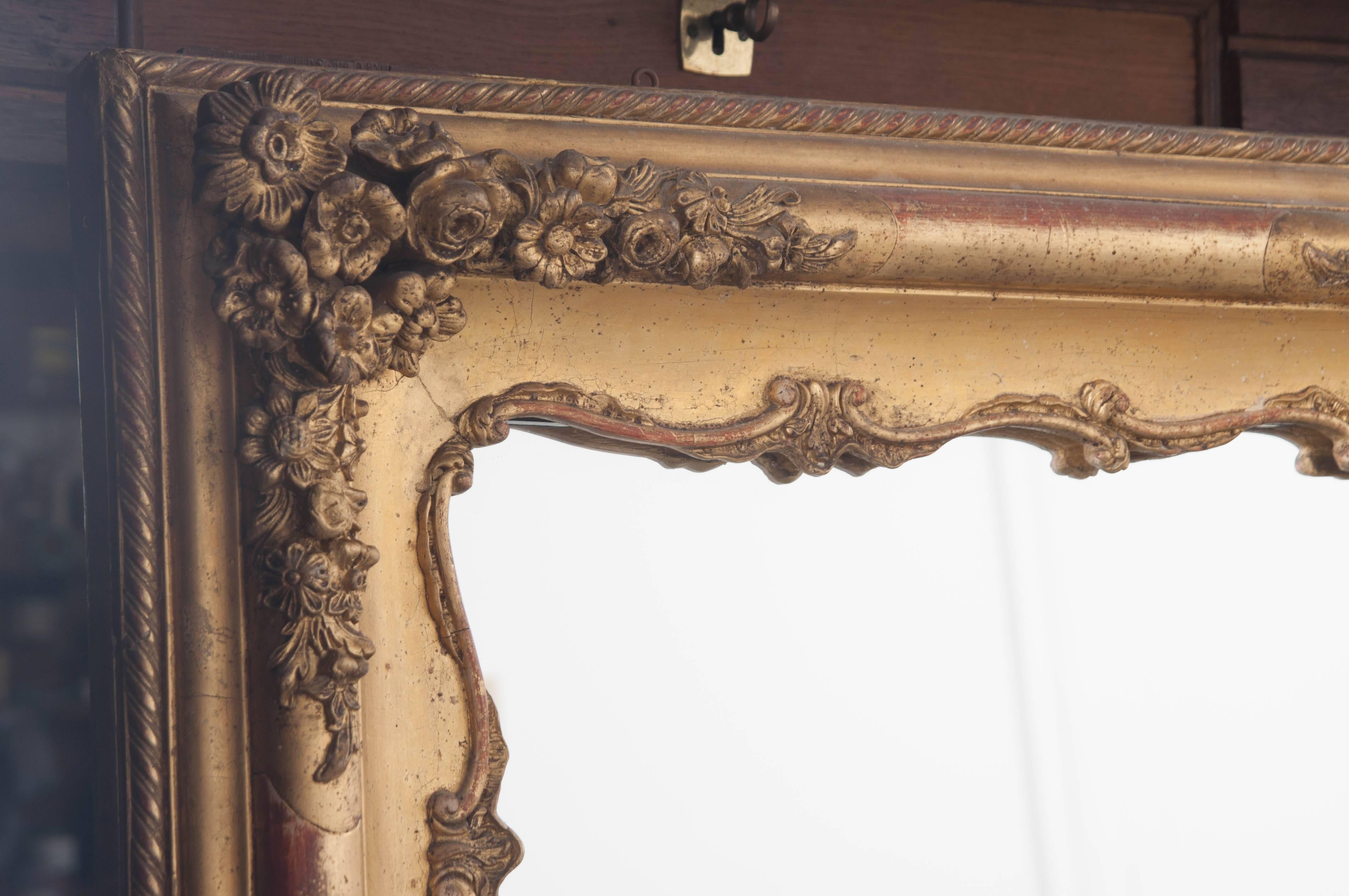 A marvelous mantel mirror, finished in beautiful gold gilt, from 19th century, France. This ornately decorated mirror boasts many design features. All four corners, sides and top are bedecked with intricate floral bouquets, from which leafy vines