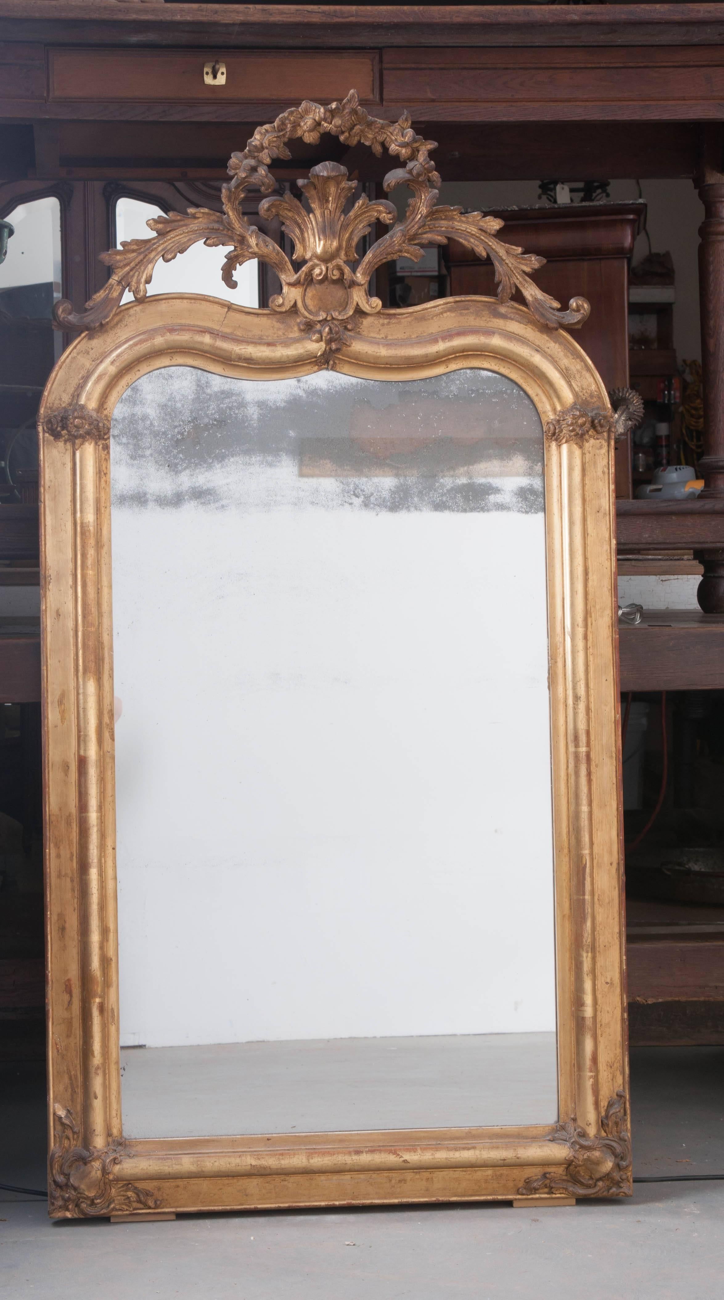 This stately mirror is finished in brilliant gold gilt and features a cartouche that is second to none! Made in France, circa 1870, this beautiful mirror has an ogee top upon which the impressive cartouche sits. It is made up of a central splay of