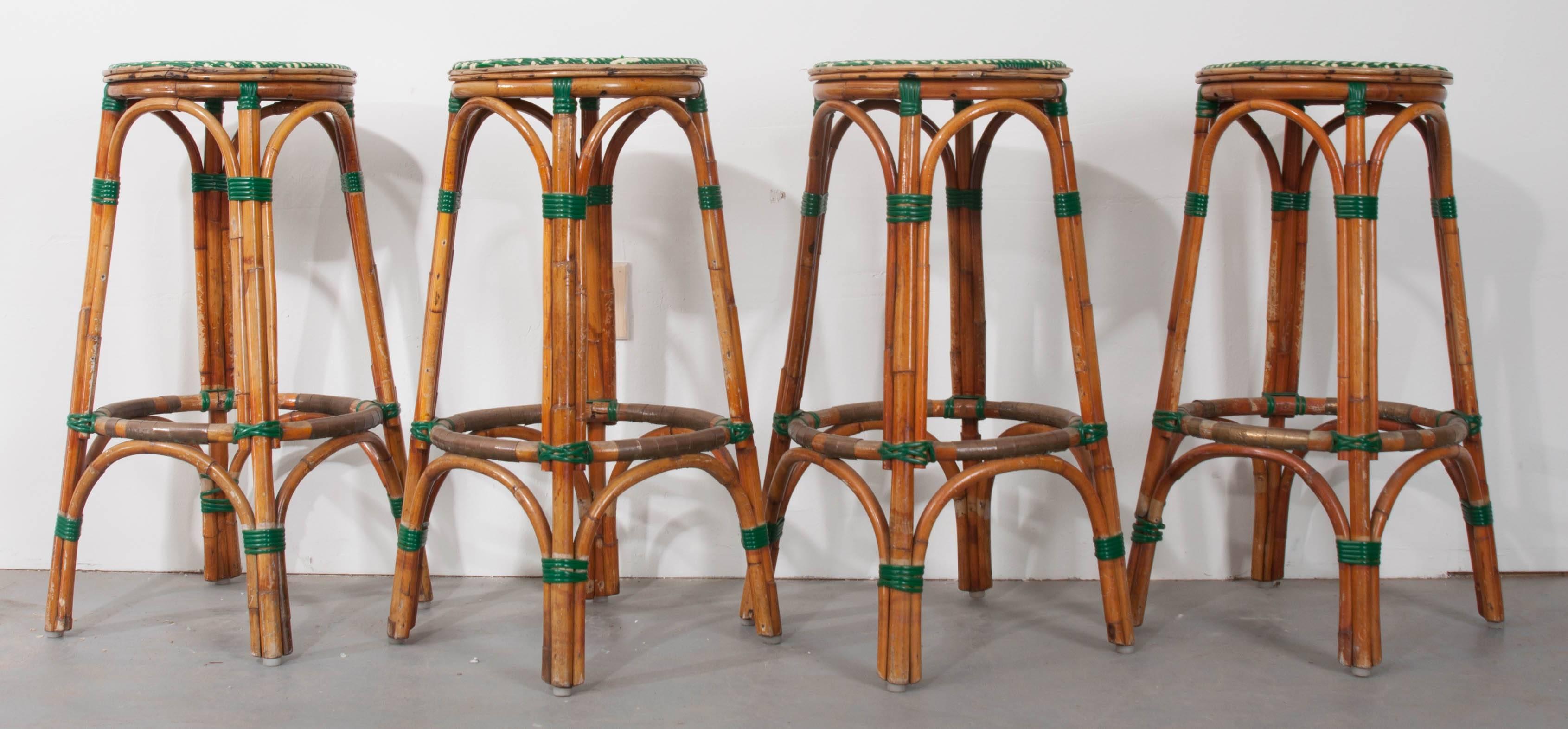 A fabulous set of four French vintage rattan bar stools with green and ivory seats and matching green banding to stabilize their bases. The Classic style of these bistro stools is quintessentially French. Measures: The stools have seats with a