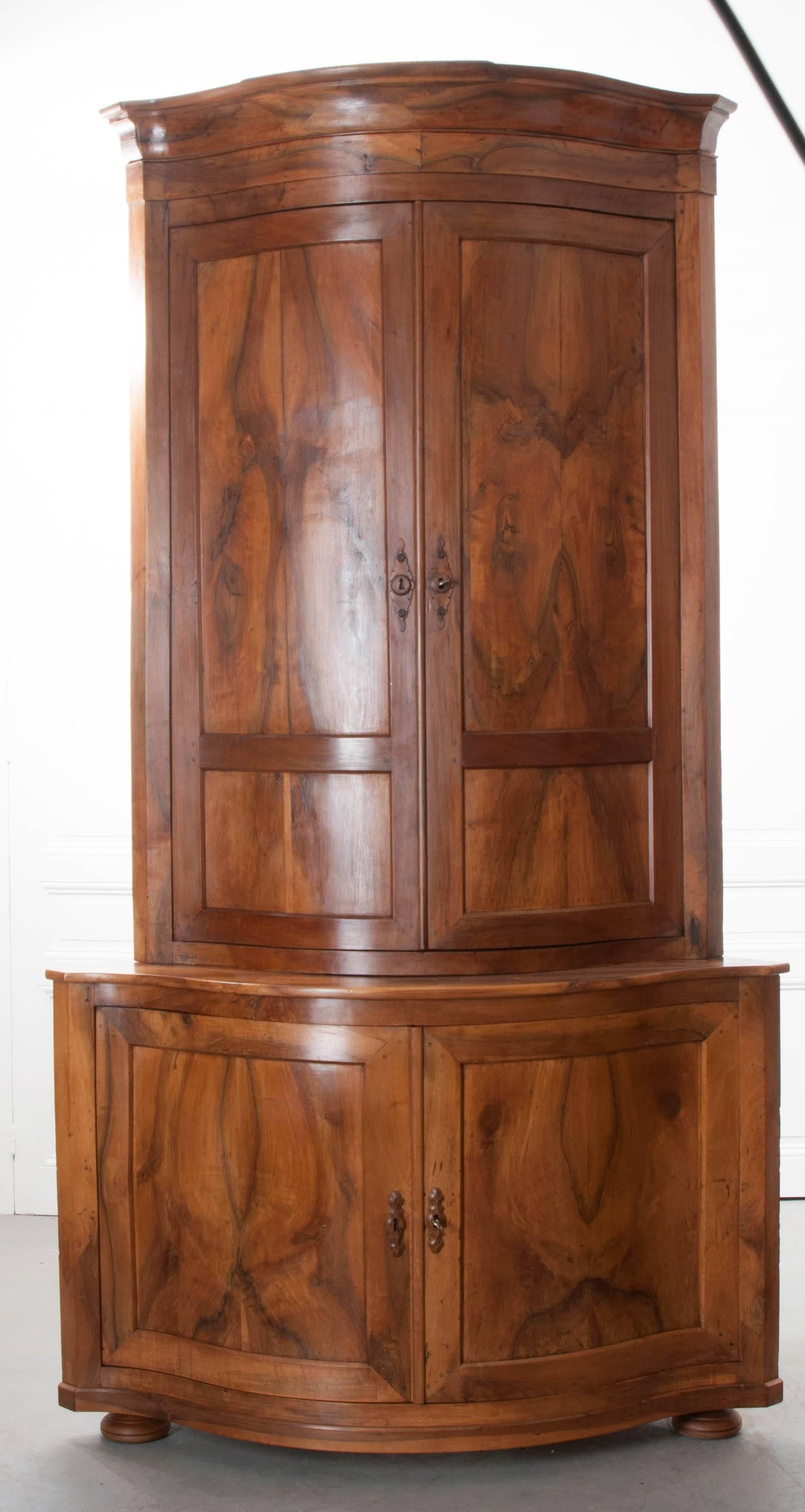 A striking pair of walnut buffet a’deux corps corner cabinets from 19th century France. These beautiful antique cabinets have gracefully curved fronts that give them a distinct, stylish appearance, and also maximize the space available inside for
