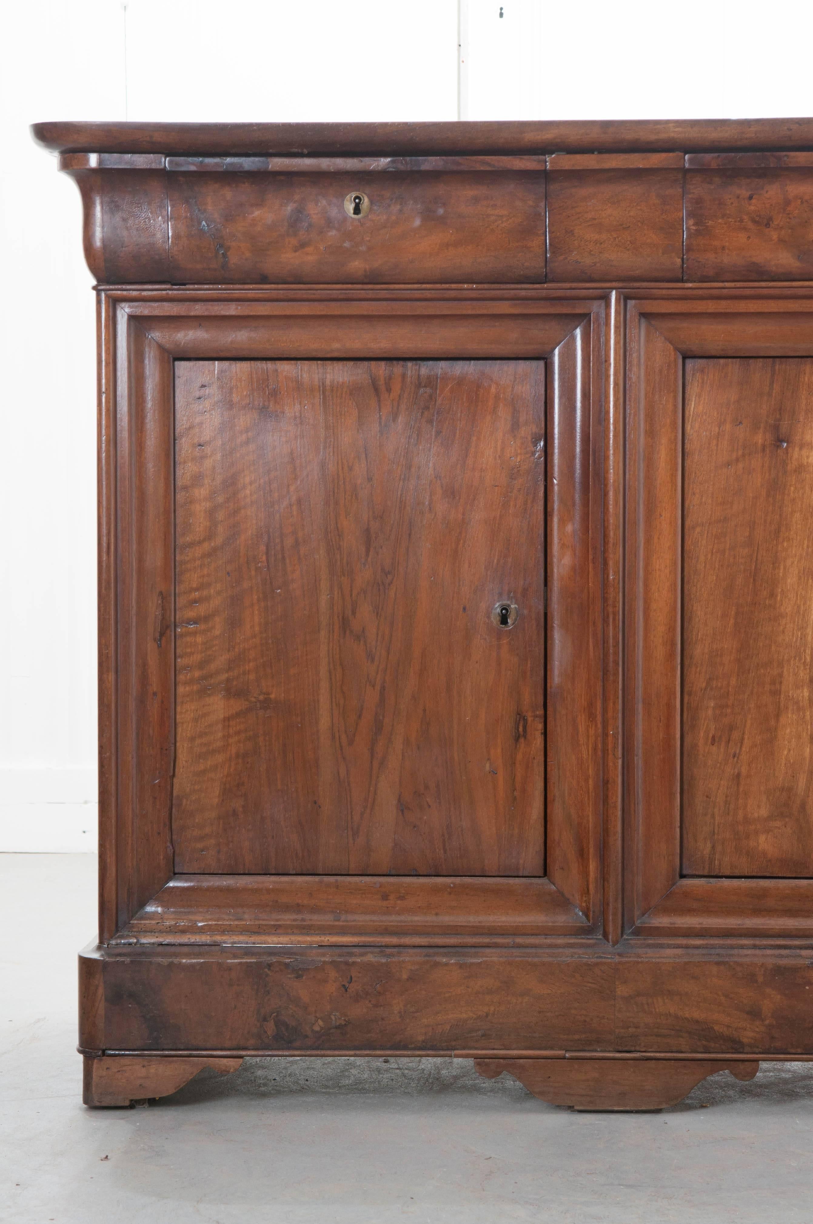 A terrific four-door walnut Louis Philippe enfilade from 19th century, France. This antique enfilade has three drawers, all containing working locks, that are positioned above four doors, which close before three separated interior cavities. The