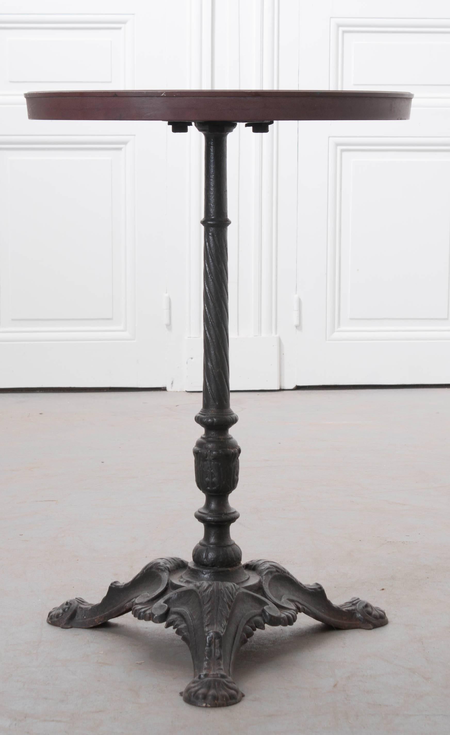An excellent cast iron bistro table from 1920s, France. The iron tripod base is done with a Classic styling and has a marvellously aged patina. The burgundy colored top is newer and was added to the base after the table was originally made. This